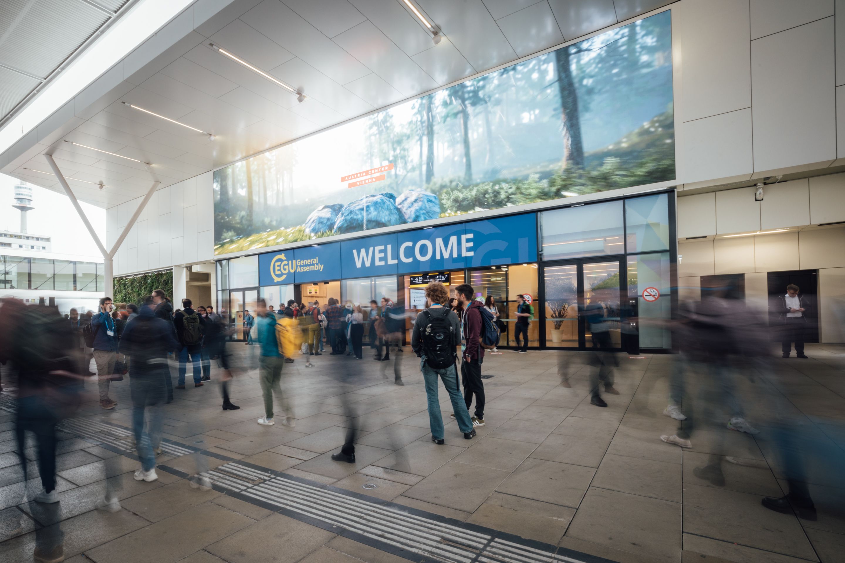 Menschen vor Eingang mit blauem Schild „WELCOME“ und „EGU General Assembly“
