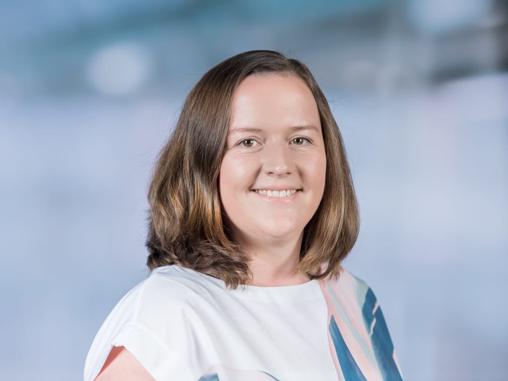 Person with shoulder-length brown hair wearing a white top with blue and pink patterns