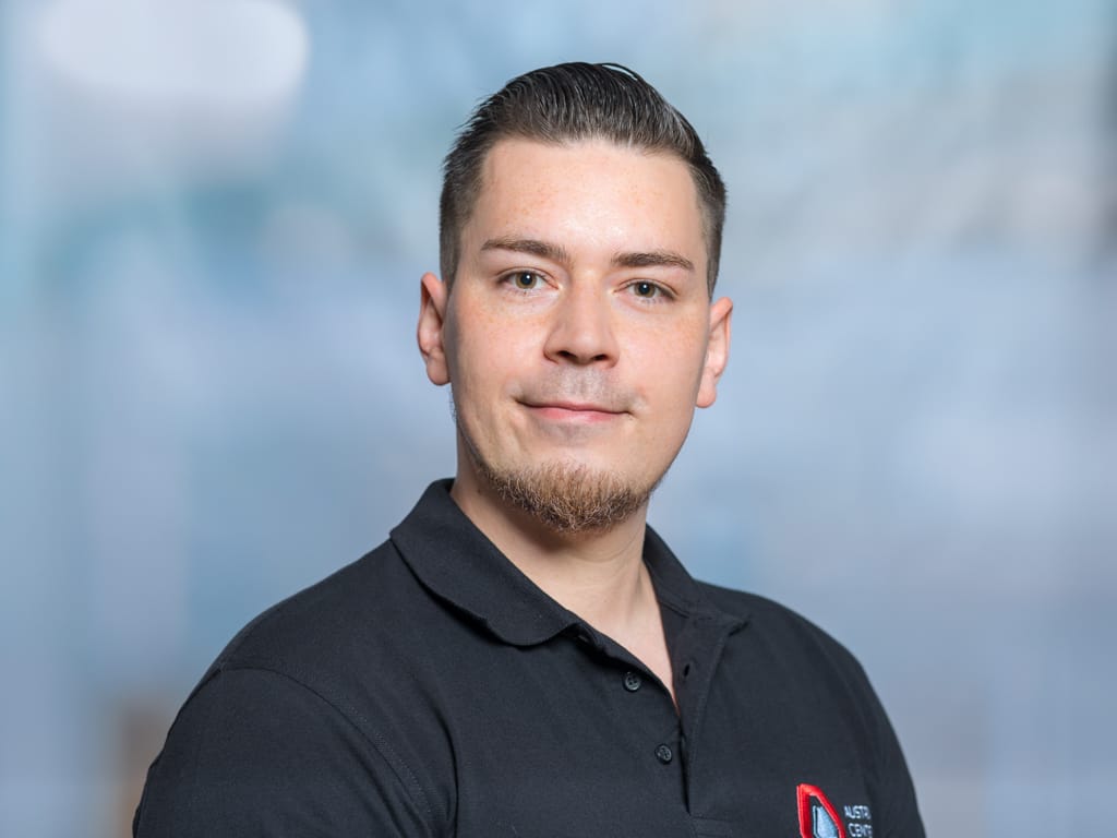 Man wearing black polo shirt with a red and white logo on the chest against a blurred background