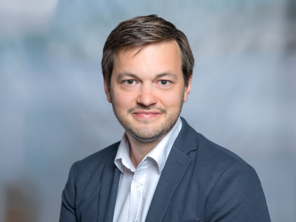 Man wearing a white shirt and dark blue blazer against a gray background