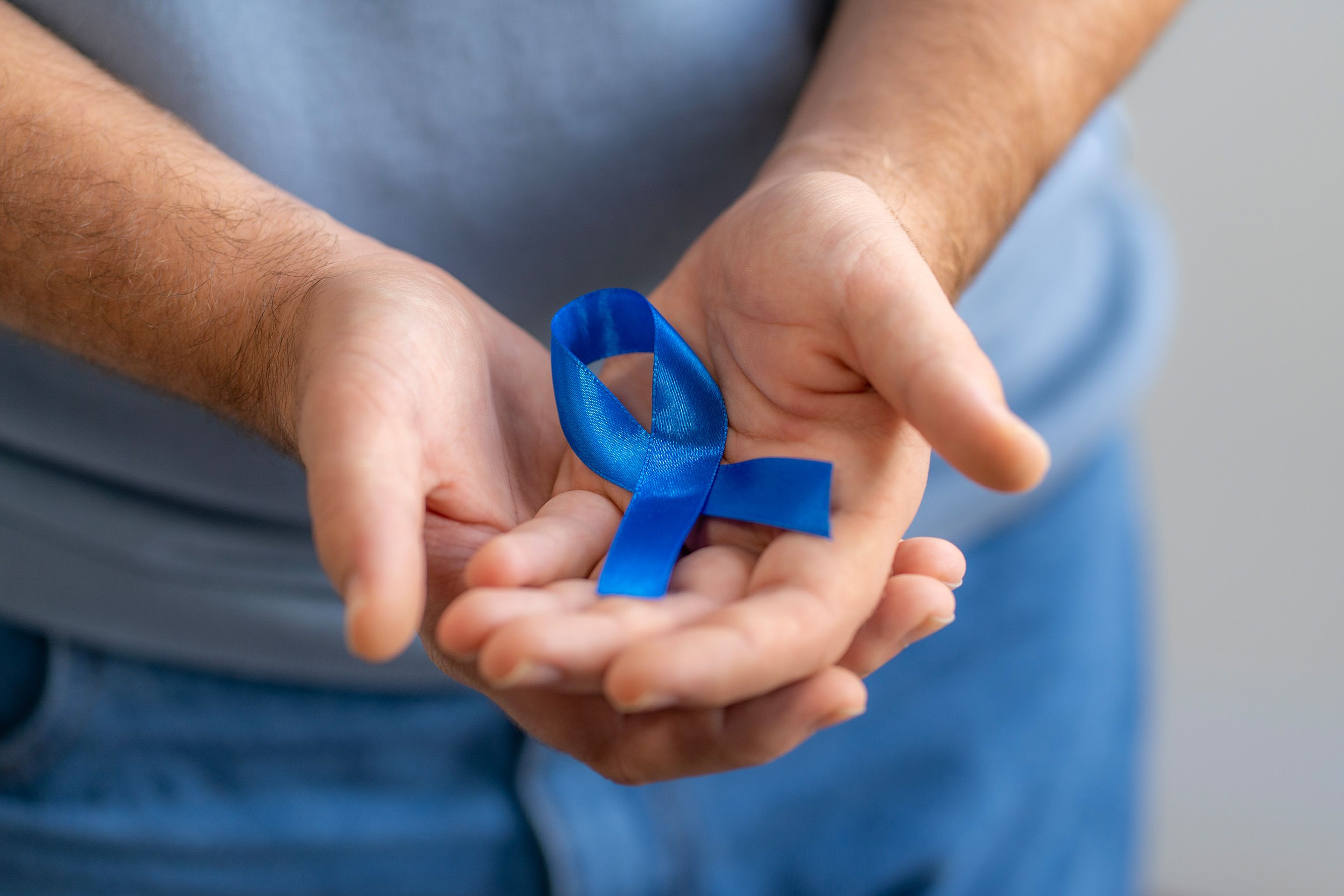 Hands holding a blue awareness ribbon against a blurred background