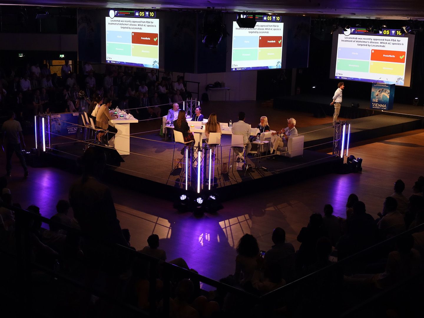 Podiumsdiskussion mit mehreren Personen und Präsentation zu Alzheimer-Behandlung auf Leinwand