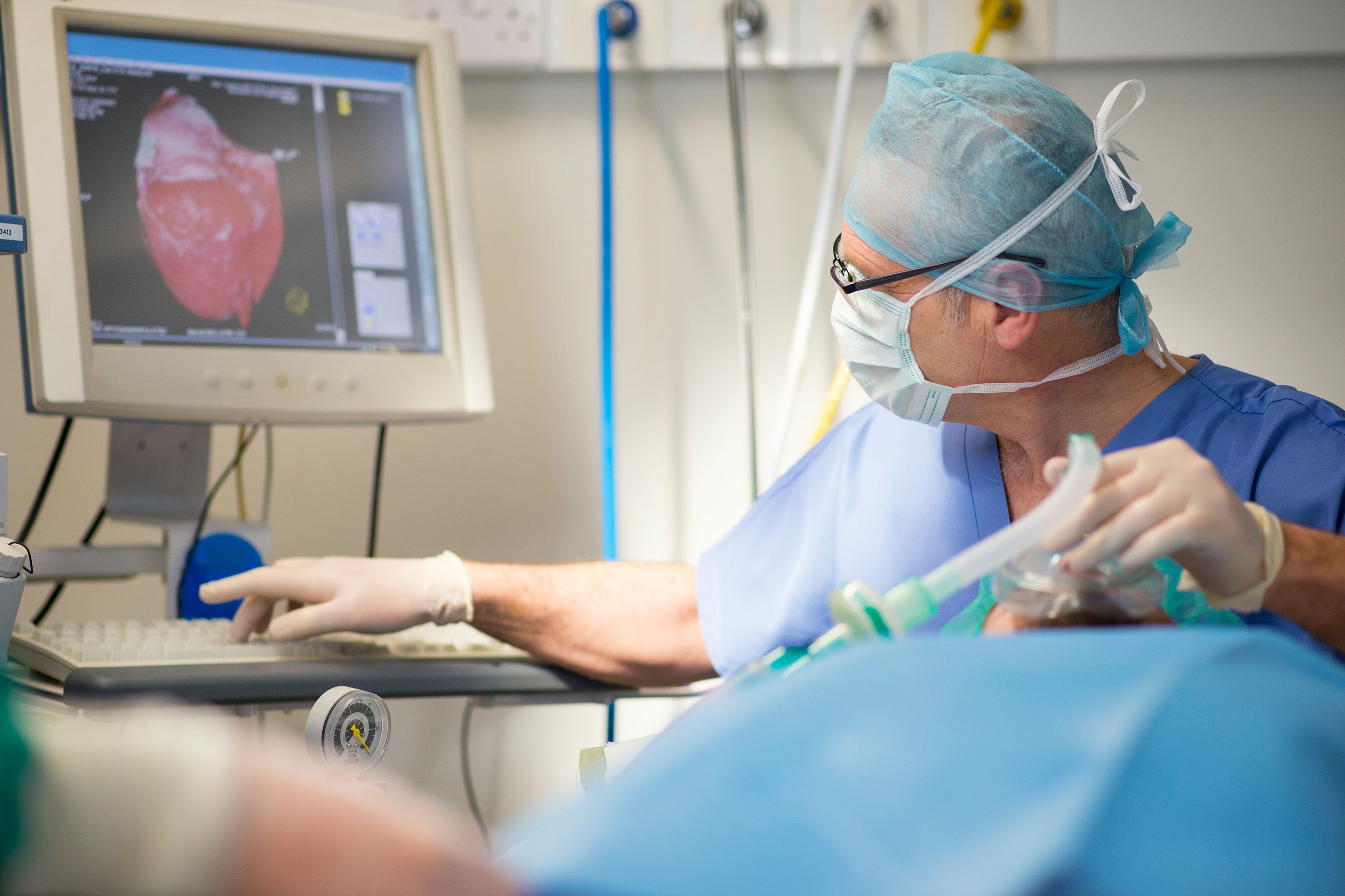 Medical professional in scrubs and gloves operating a computer with a heart image on the screen