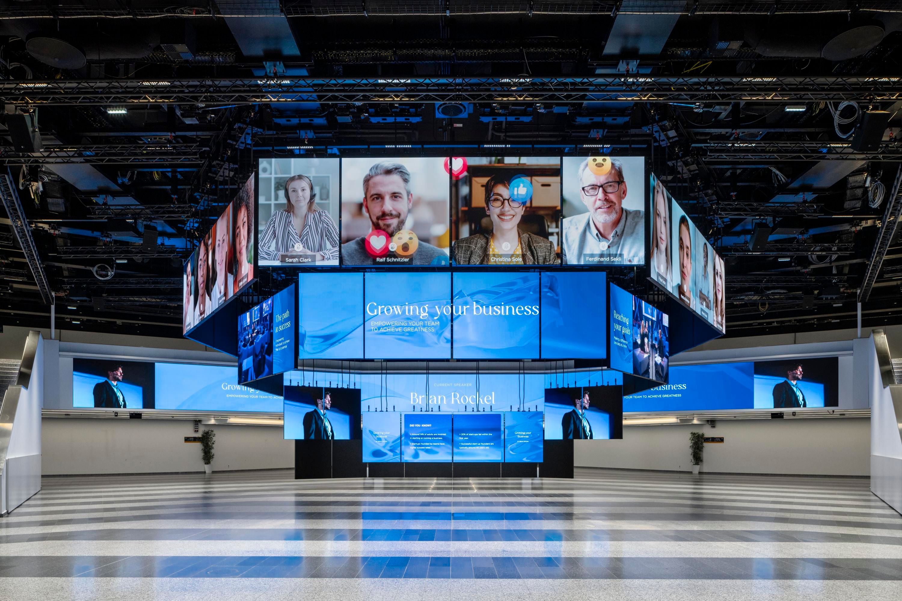 Large digital display with business presentation and video call participant images above it.