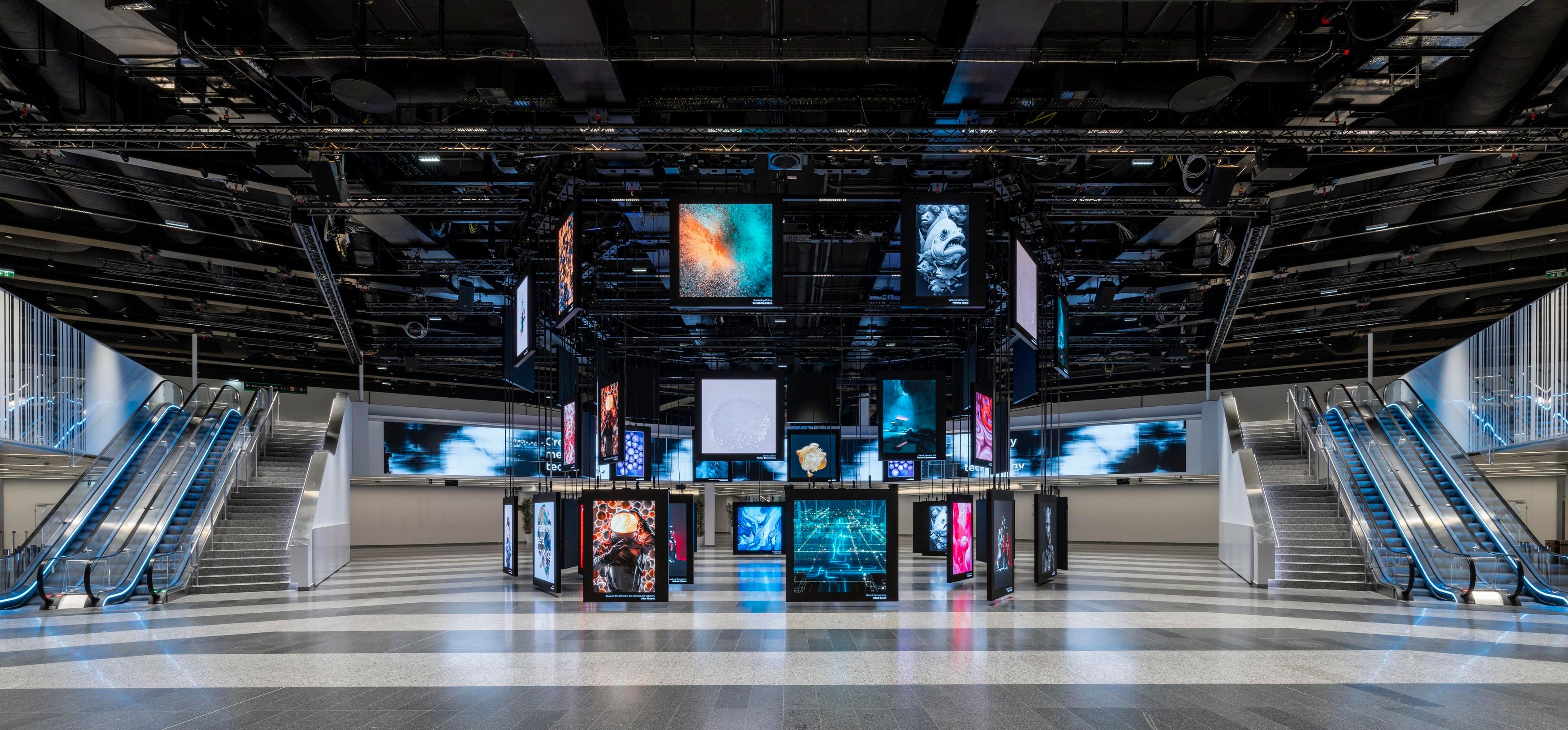 Modern exhibition space with multiple digital screens suspended and escalators on both sides
