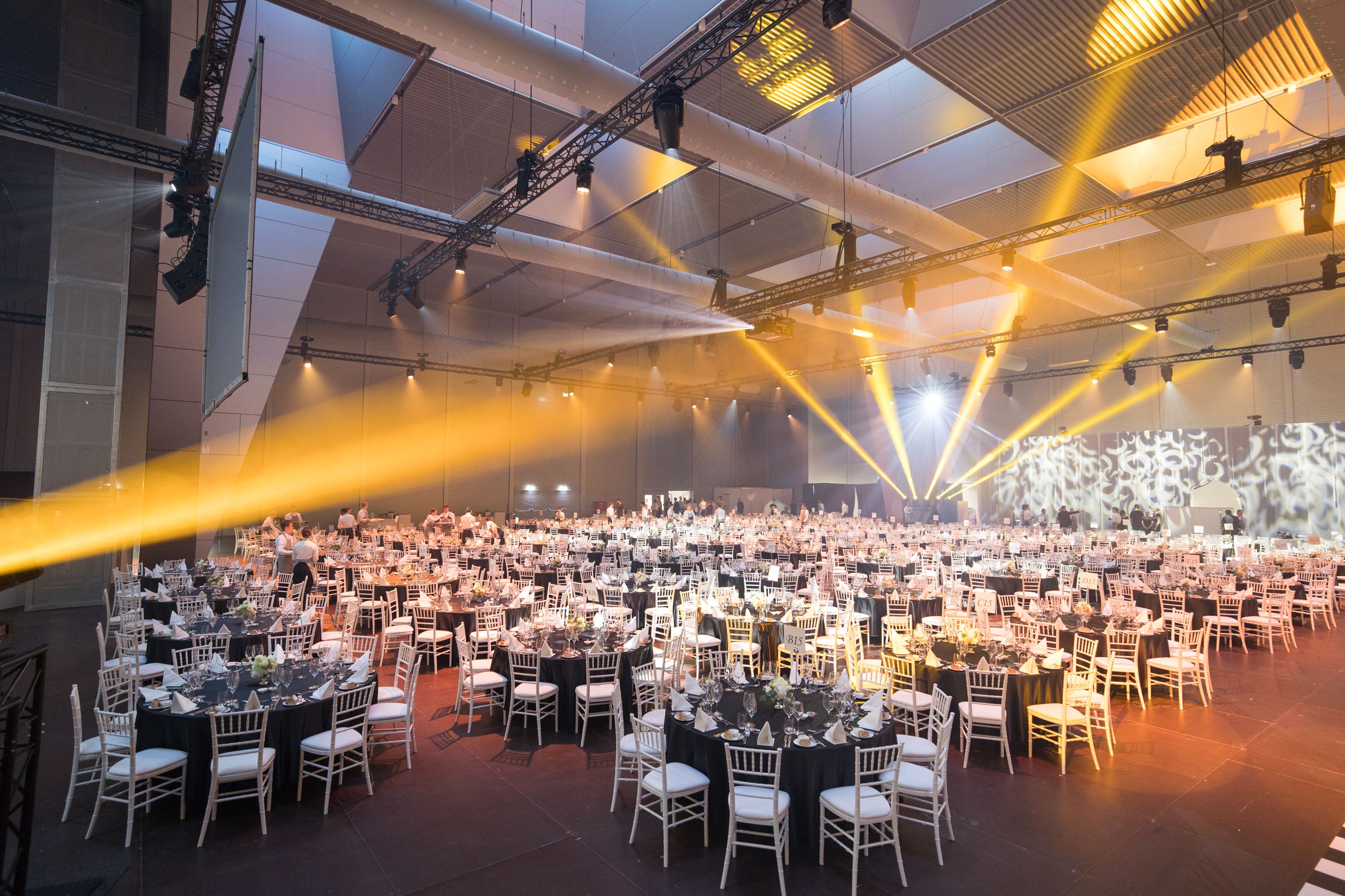 Large banquet hall with round tables set for dining and yellow stage lights