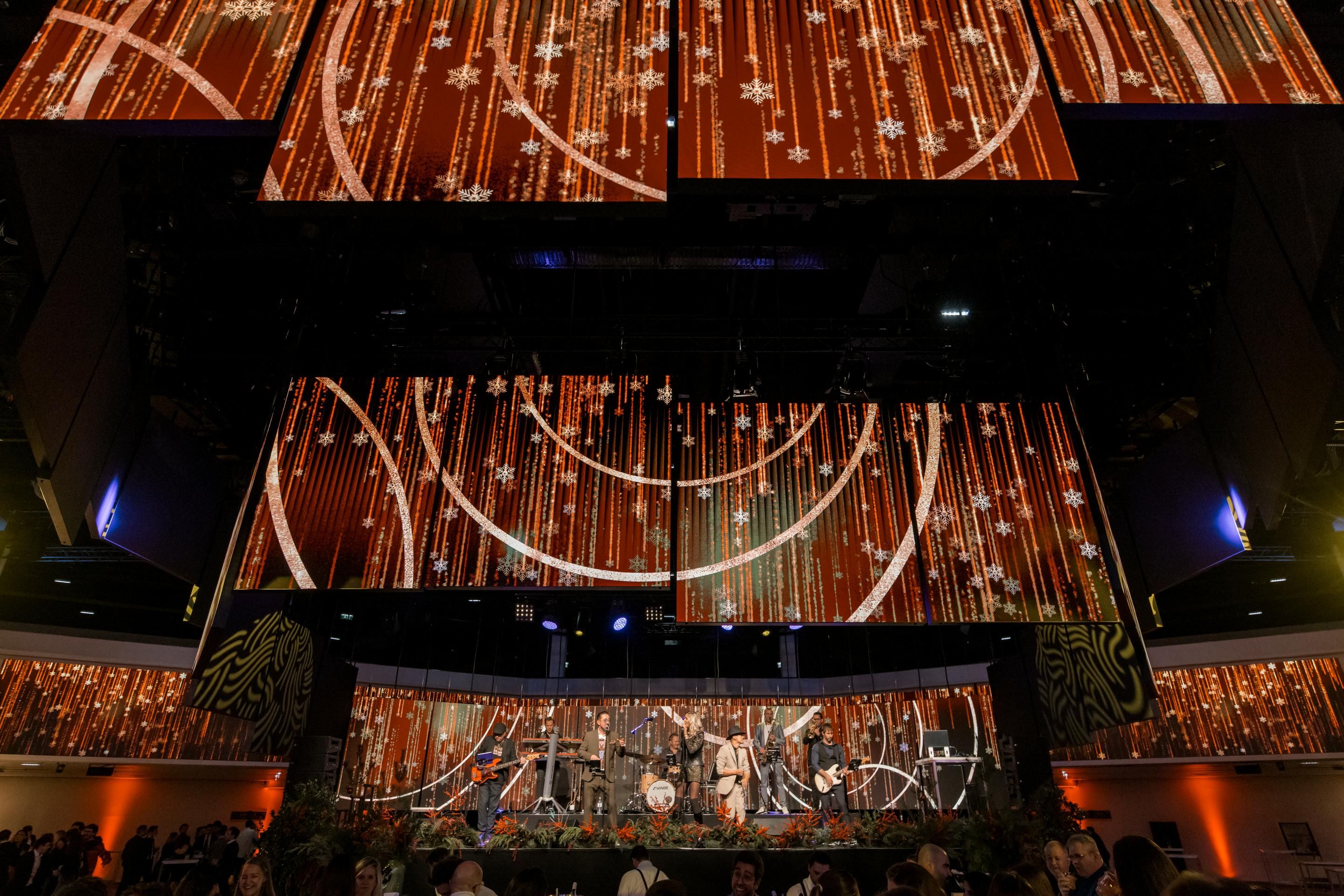 Bühne mit Band und orange-weißem Lichtdesign, Publikum im Vordergrund