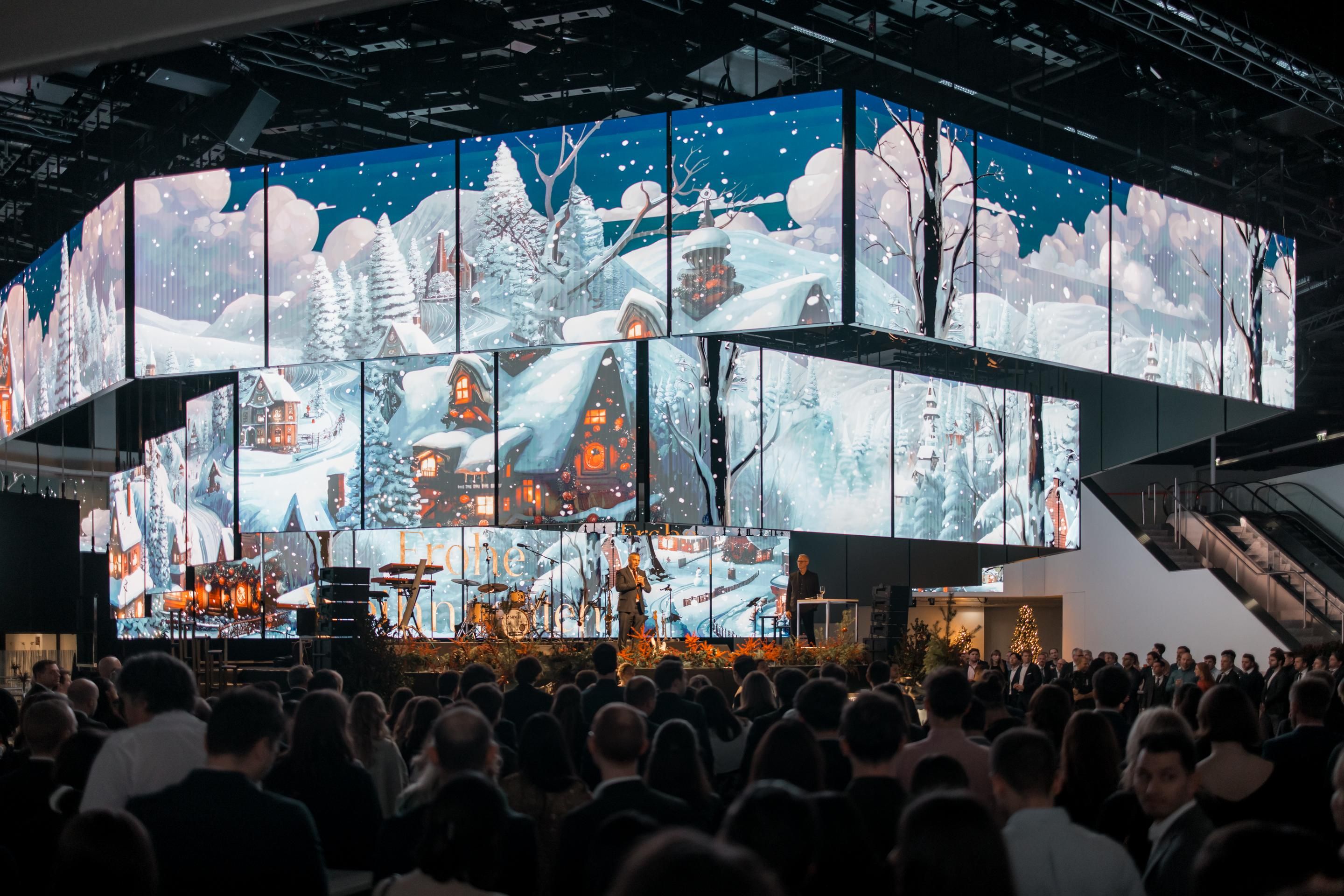 Große LED-Bildschirme mit Winterlandschaft und Menschen bei einer Veranstaltung.