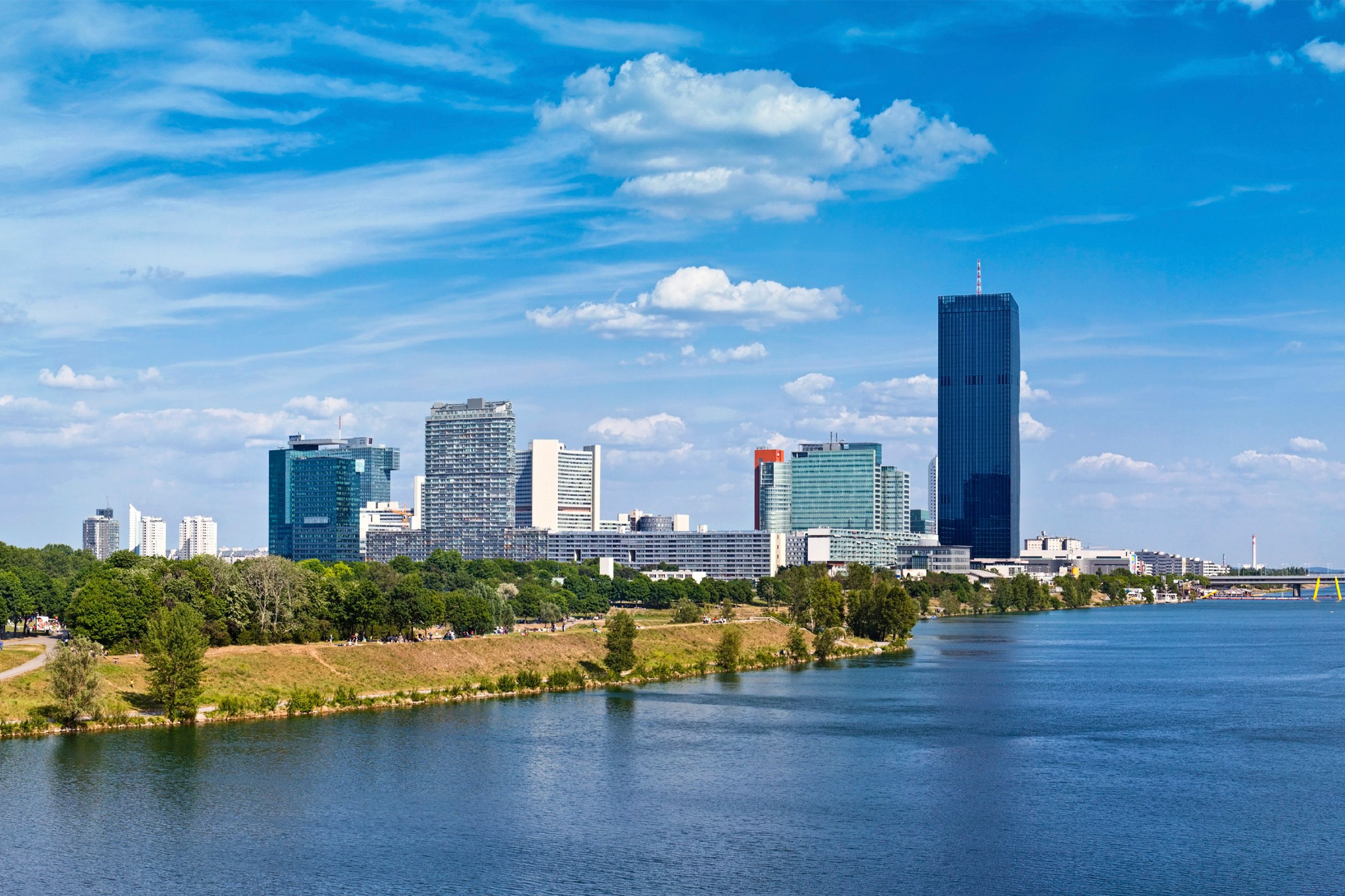 City skyline with modern buildings along a river under a partly cloudy sky