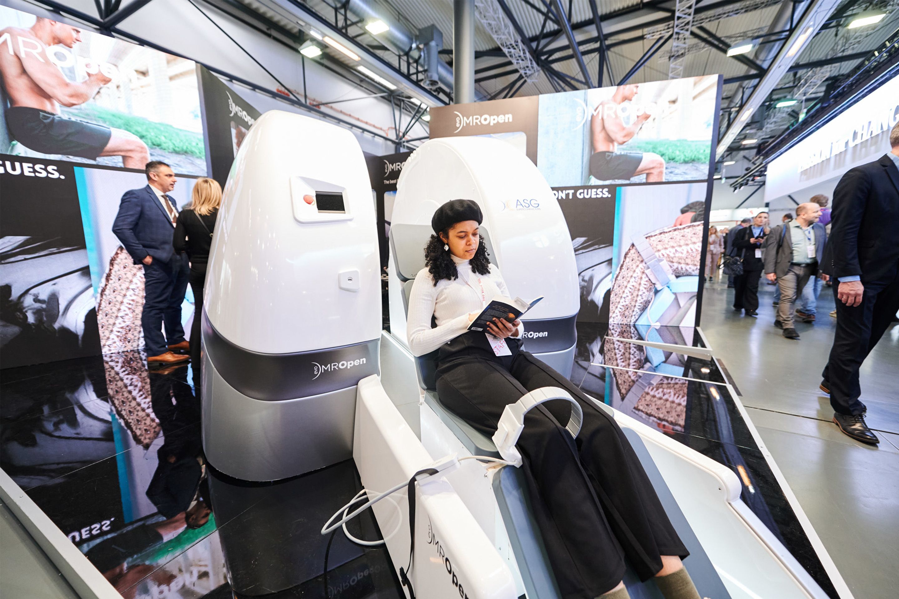 Person sitting in a medical imaging machine labeled MROpen reading a booklet at an exhibition.