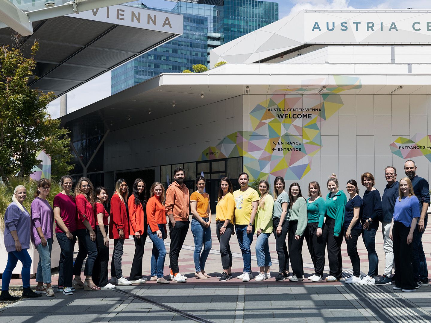 Group of people standing in a line outside Austria Center Vienna with colorful entrance signs visible