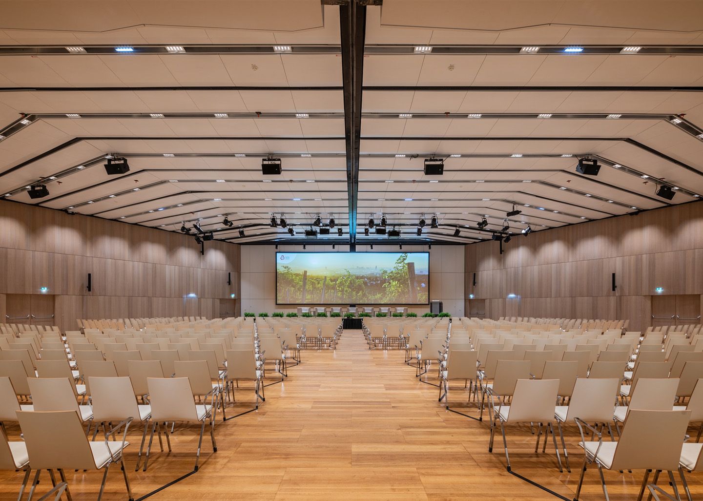 Empty conference room with rows of chairs facing a large screen and stage