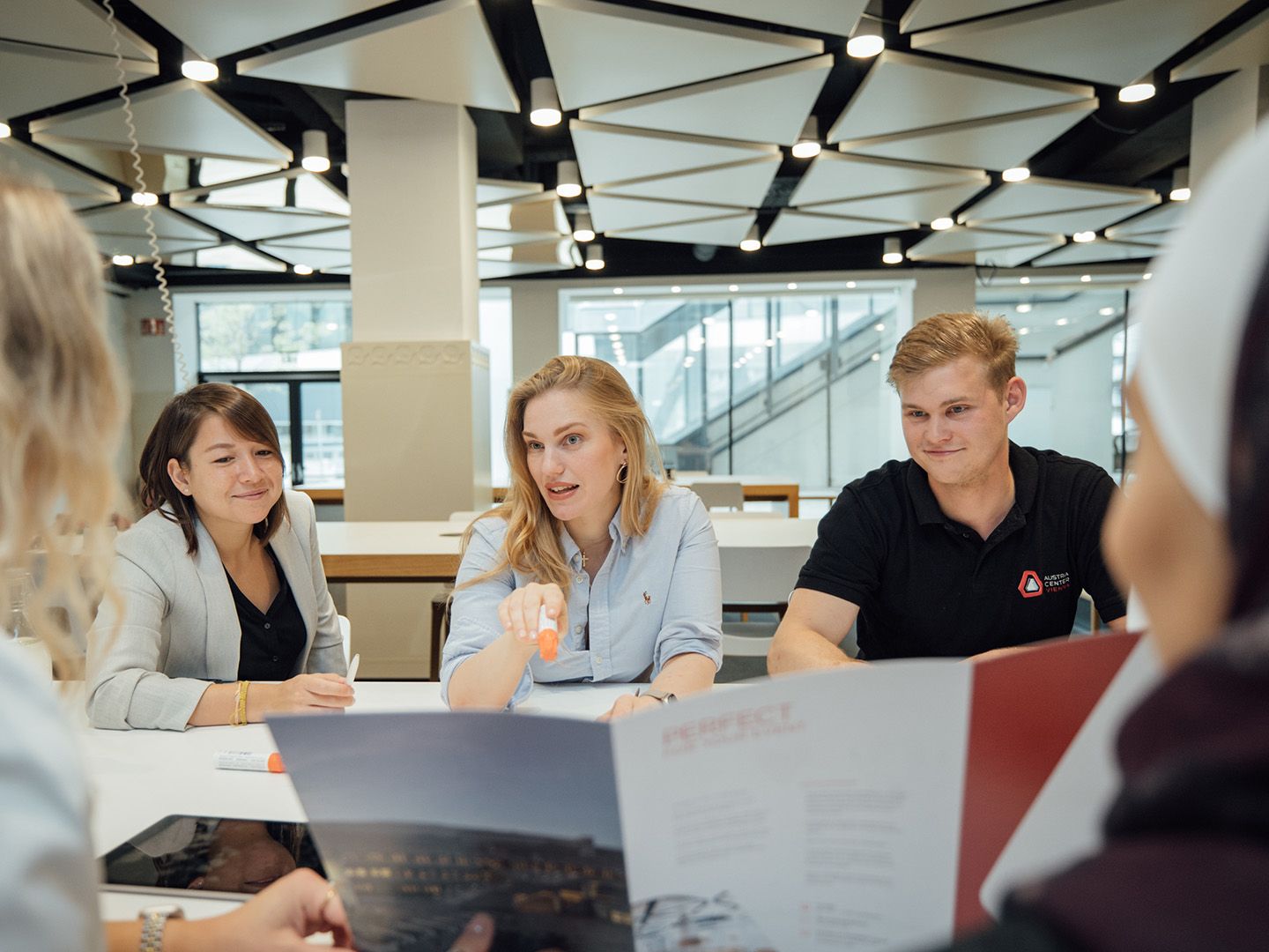 People sitting around a table in a modern meeting room with documents and a tablet.