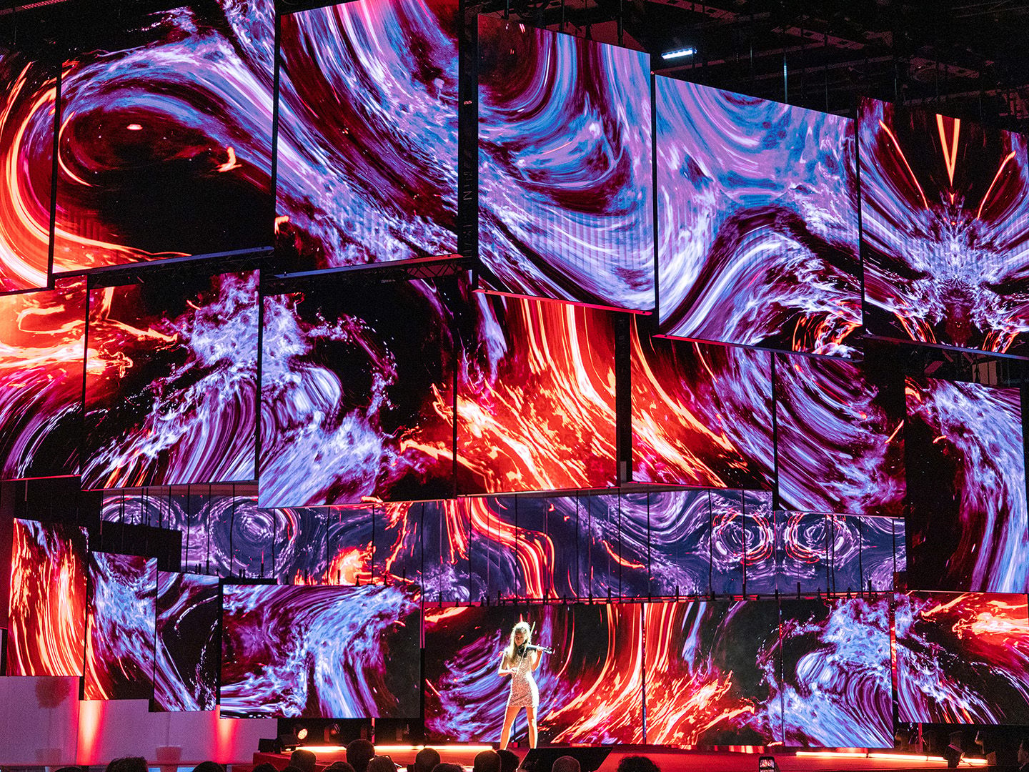 Multiple large screens with swirling red and purple abstract patterns behind a person playing violin on stage