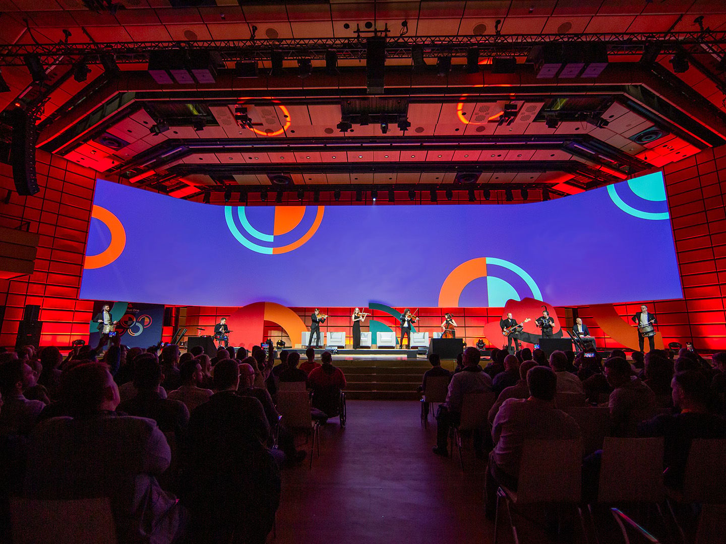 Stage with musicians performing in front of a large screen showing colorful circular patterns.