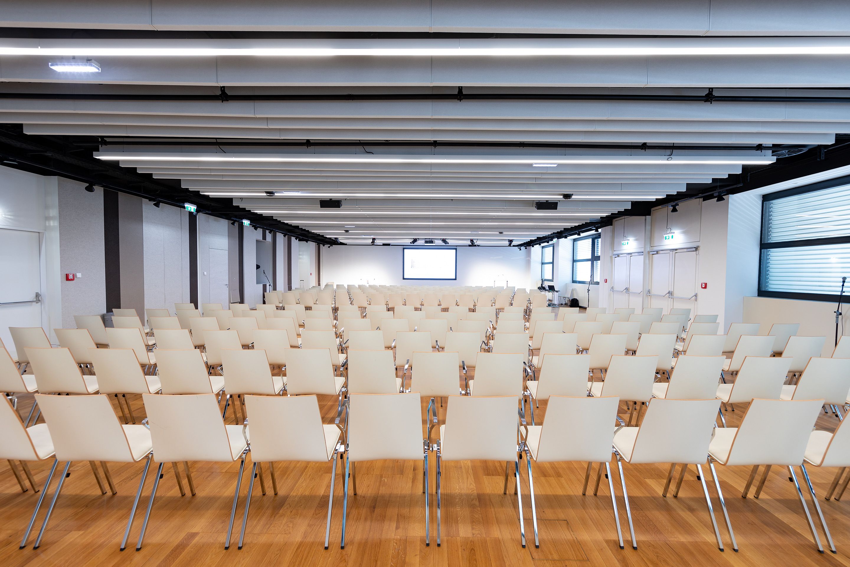 Leerer Konferenzraum mit vielen weißen Stühlen in Reihen und Projektionsleinwand vorne.