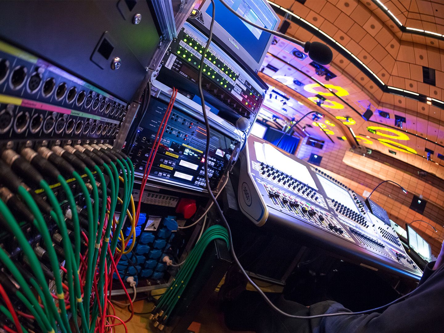 Audio mixing console and connected cables in a control room with stage lighting above