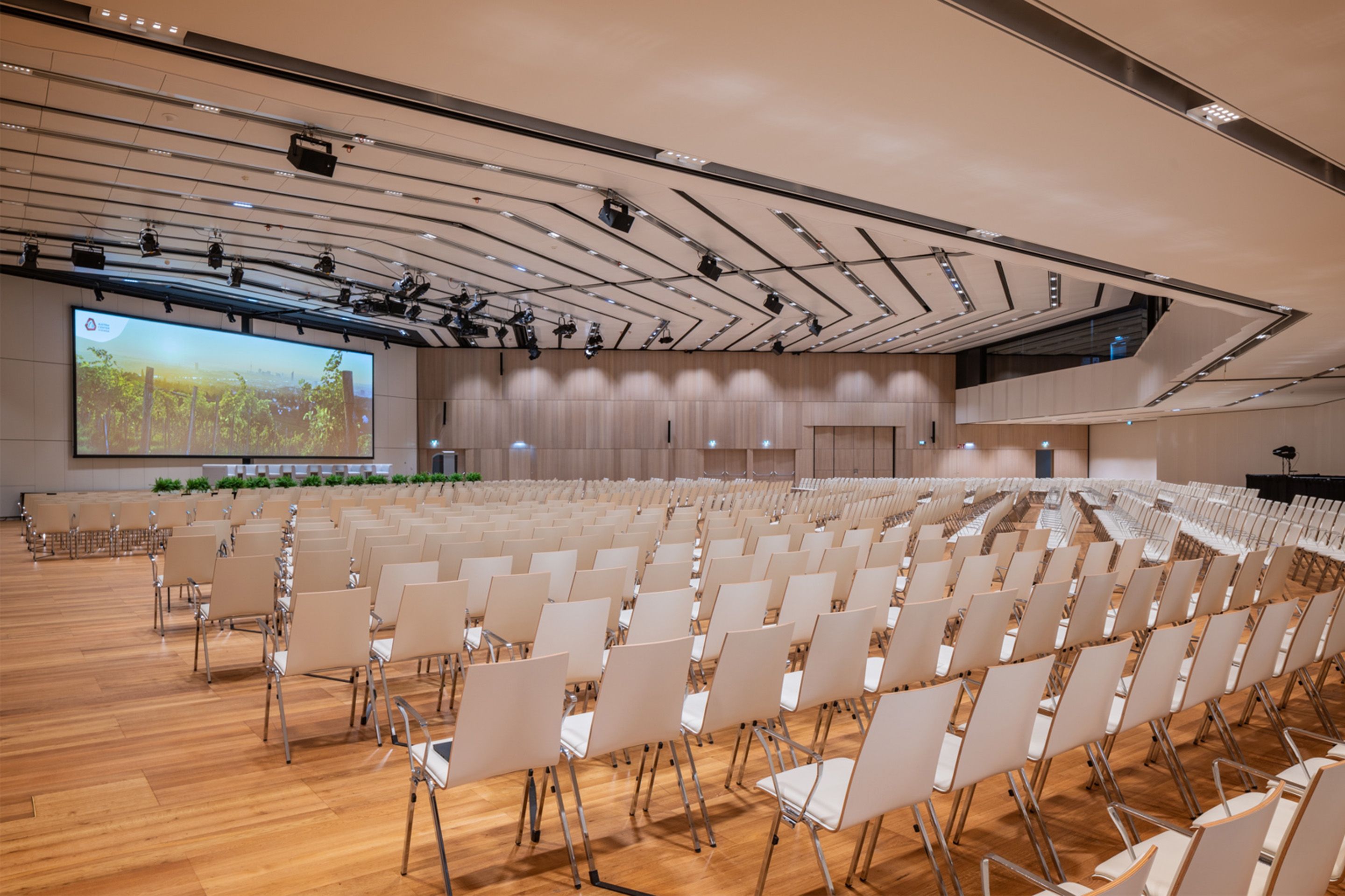 Leerer großer Konferenzraum mit vielen weißen Stühlen und einer Leinwand vorne.