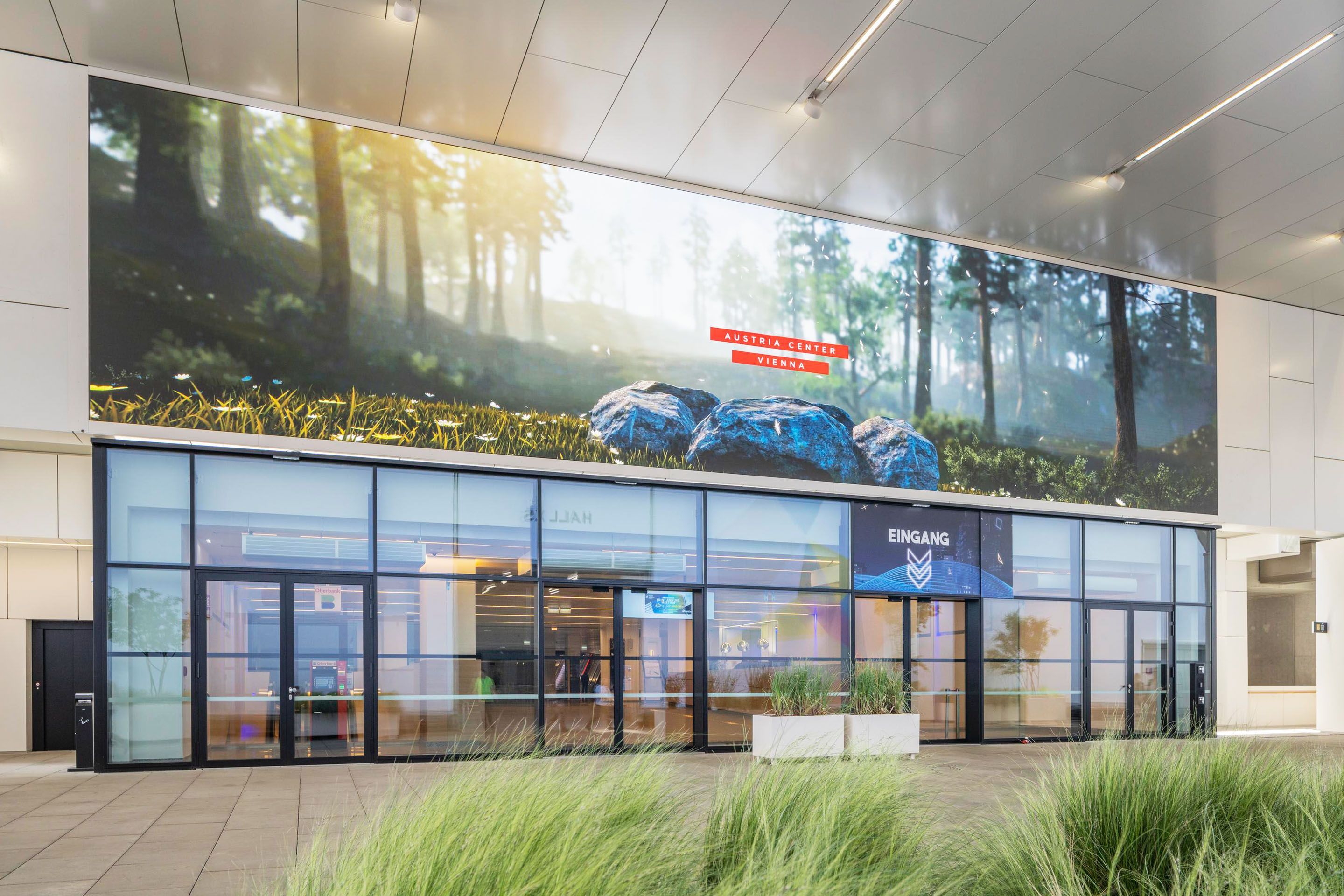 Eingang mit Glasfront und digitaler Waldlandschaft mit Text Austria Center Vienna
