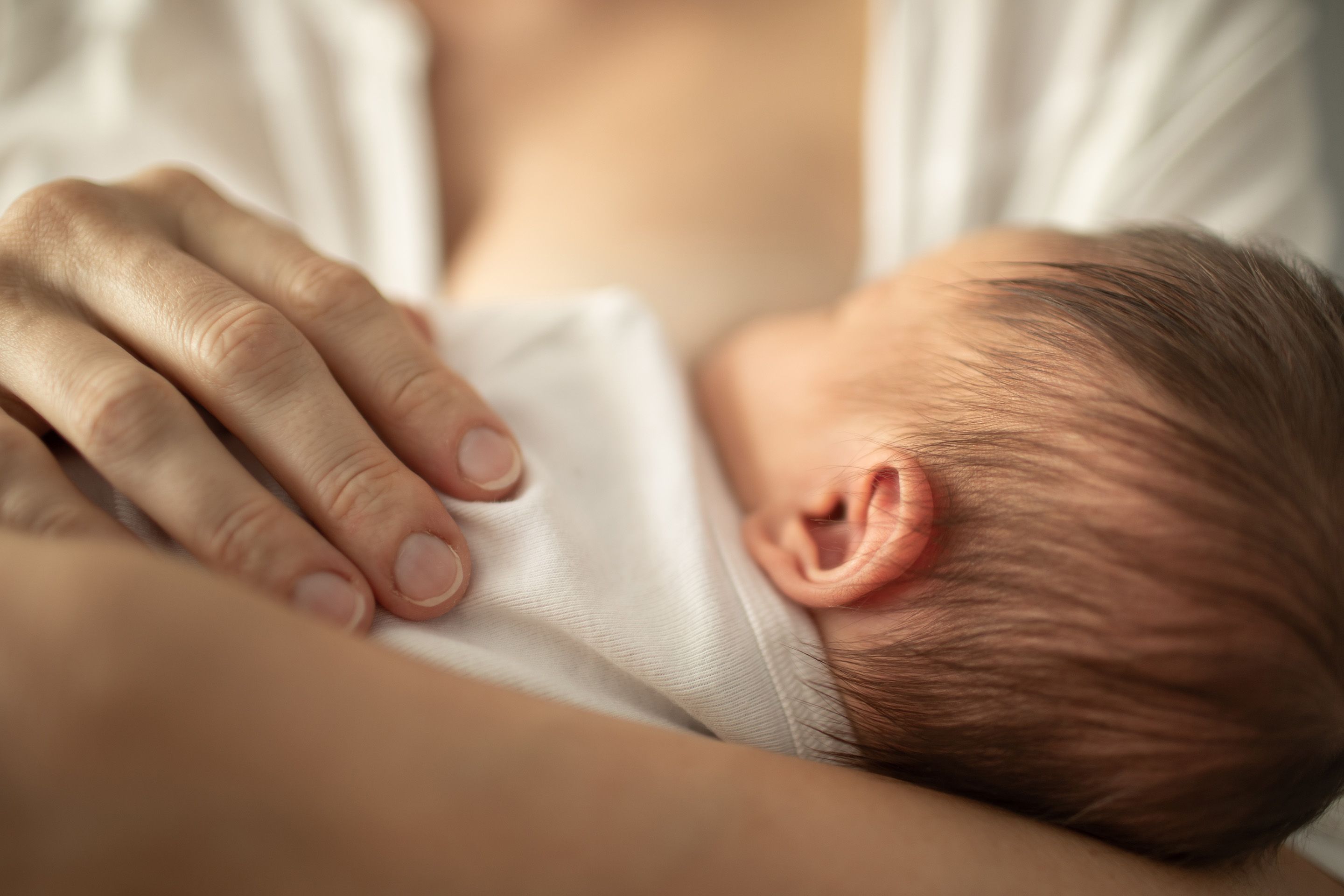 Newborn baby resting on a person's chest with a hand gently placed on the baby.