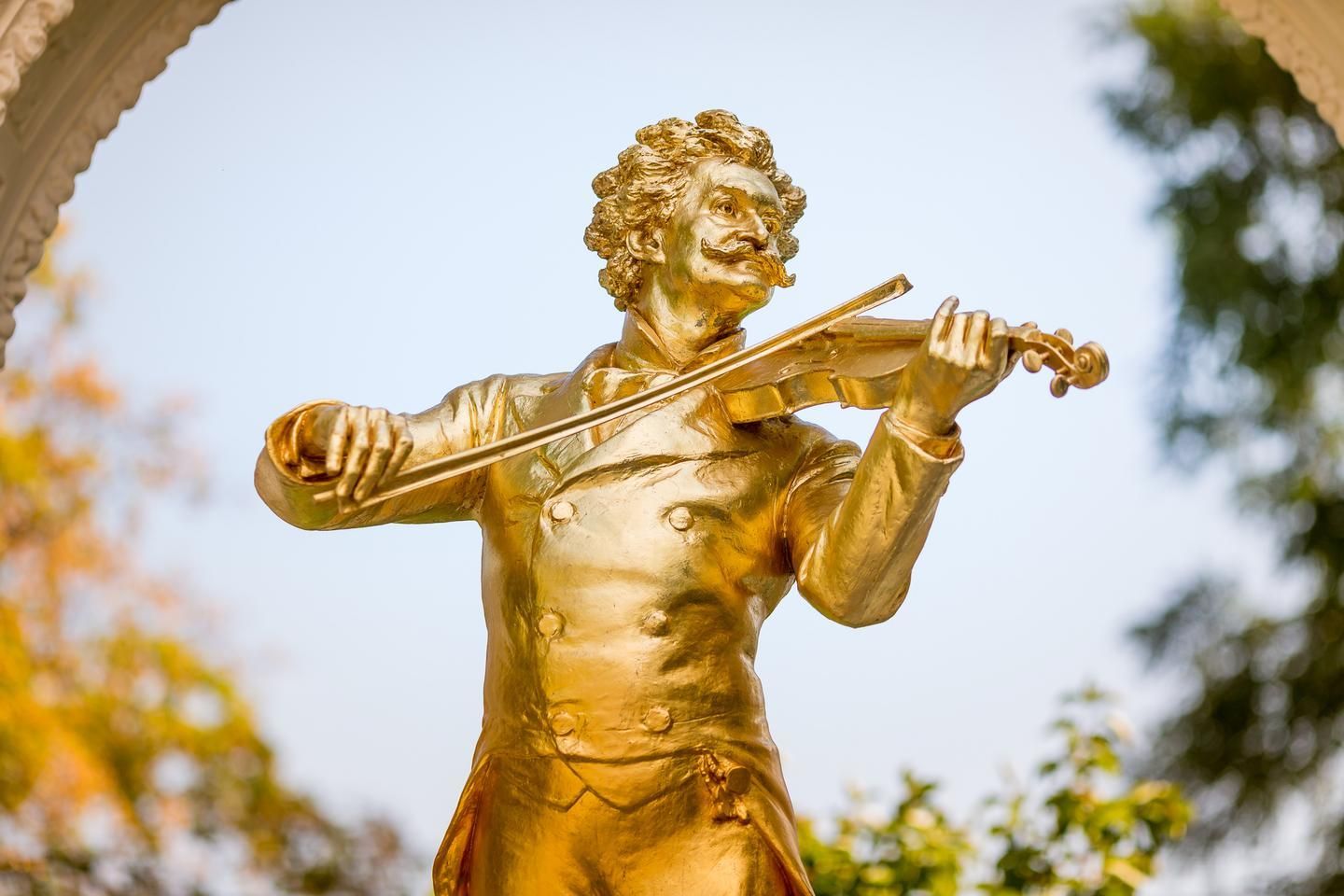 Golden statue of a man playing the violin outdoors under an archway