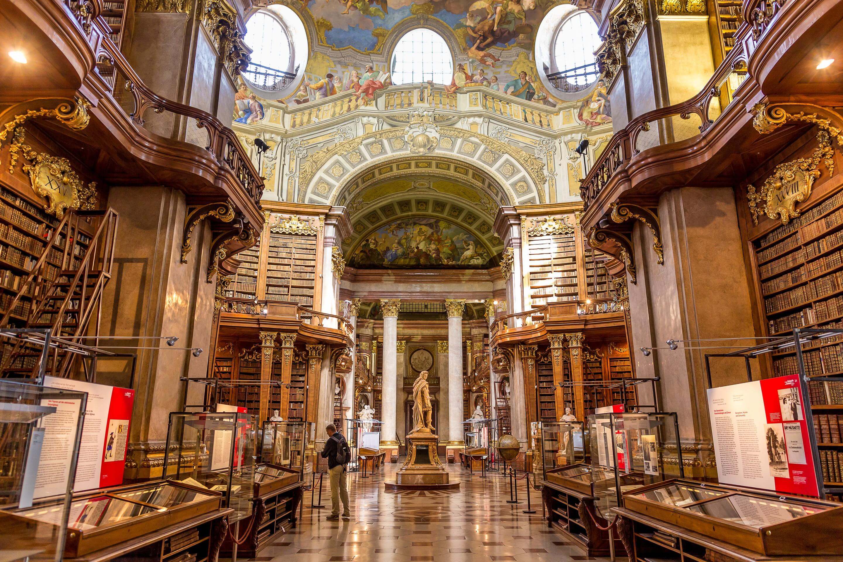 Baroque library interior with wooden shelves, statues, and ceiling frescoes