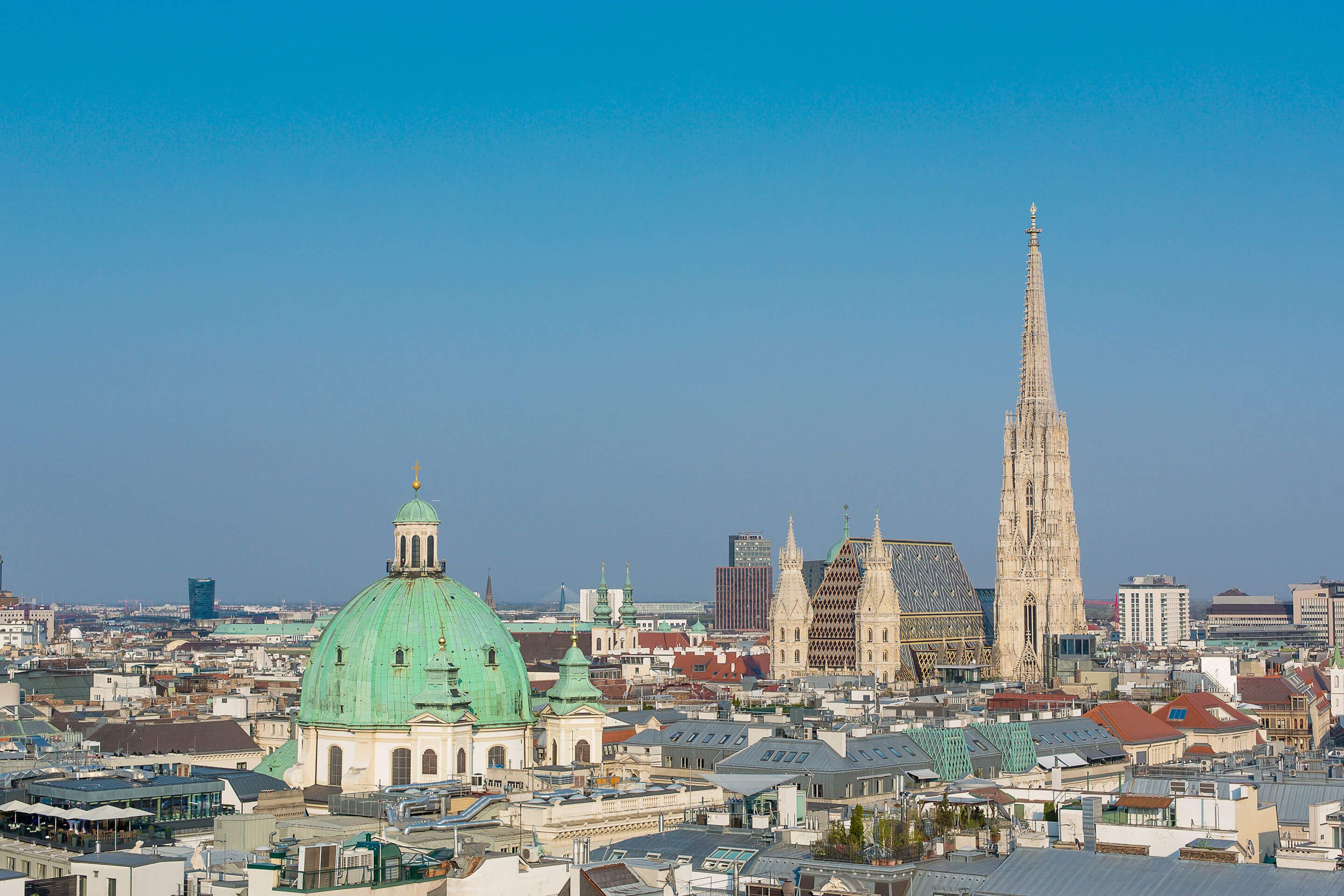 City skyline with a green-domed building and a tall Gothic cathedral spire under clear sky
