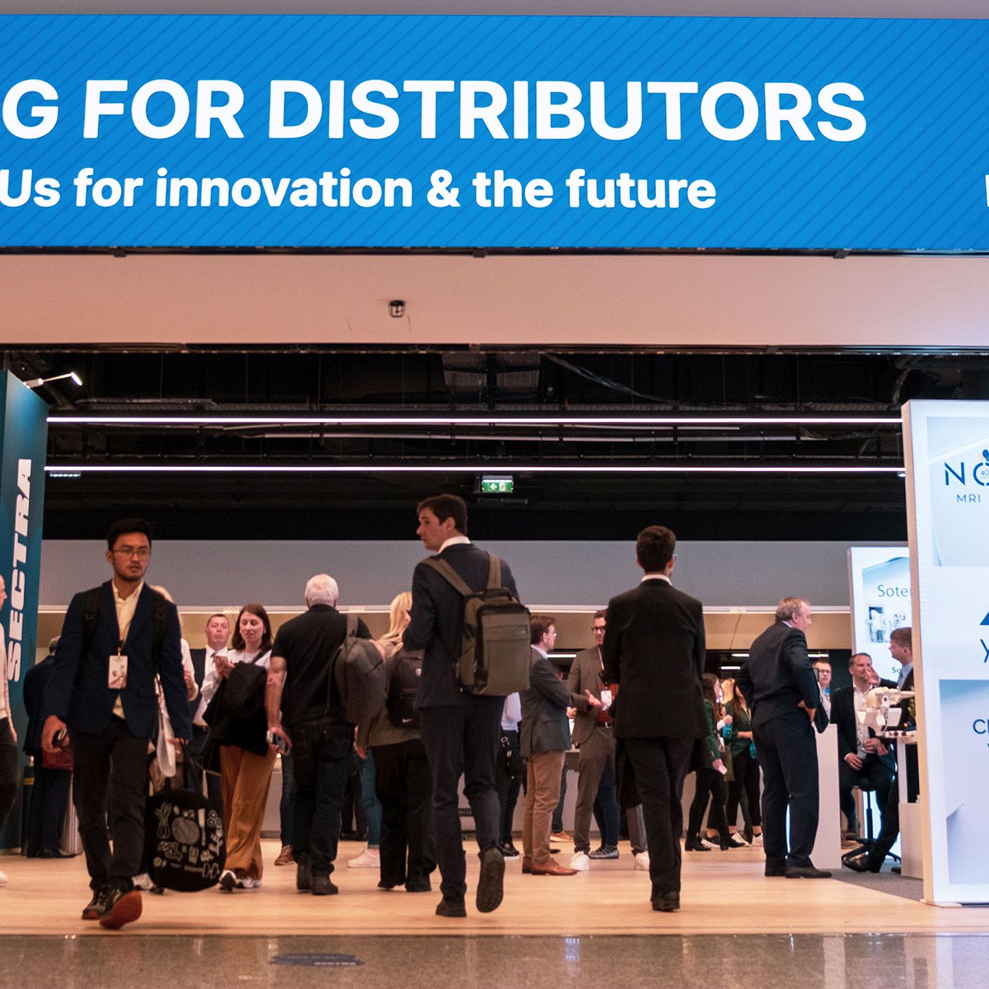 Menschen in Business-Kleidung auf einer Messe mit blauem Banner „FOR DISTRIBUTORS“ im Hintergrund.