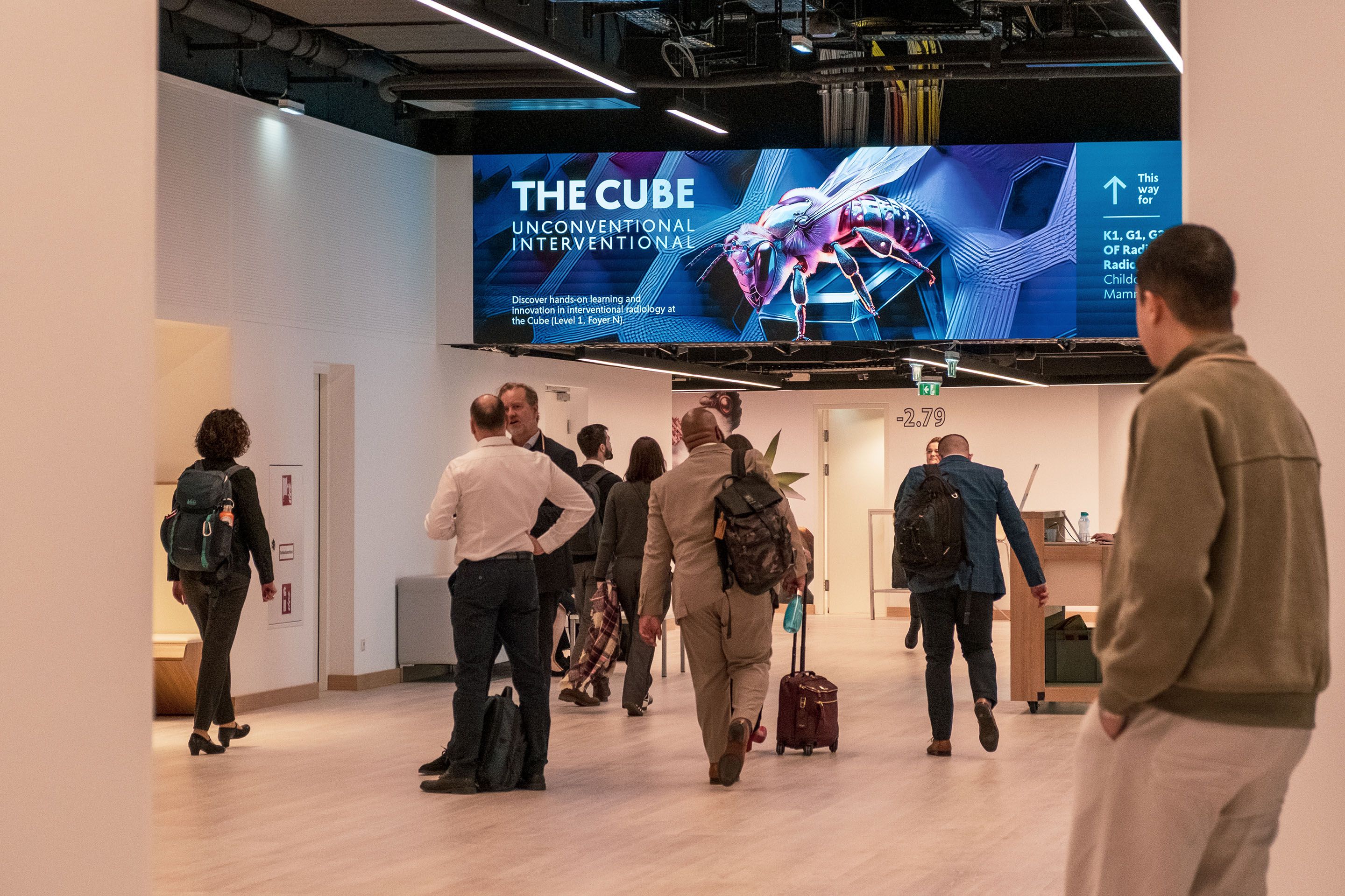 Menschen in einem Flur unter einem Schild mit Text zu „THE CUBE UNCONVENTIONAL INTERVENTIONAL“