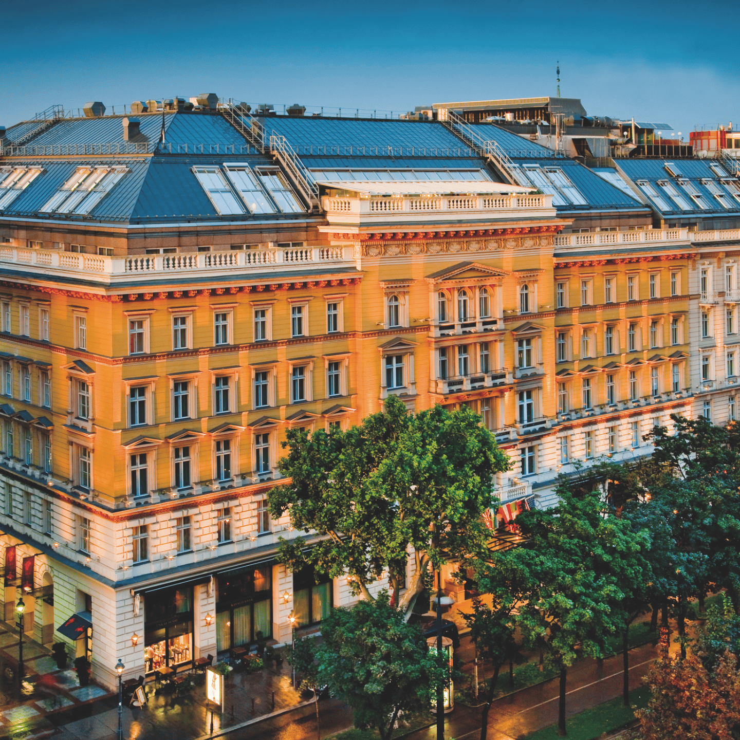 Mehrstöckiges historisches Gebäude mit vielen Fenstern und Bäumen davor bei Abendlicht