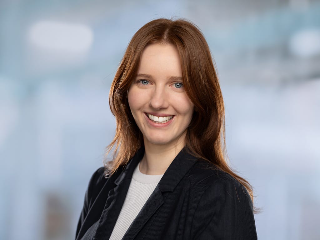 Person with long red hair wearing a black blazer and white top against a blurred background