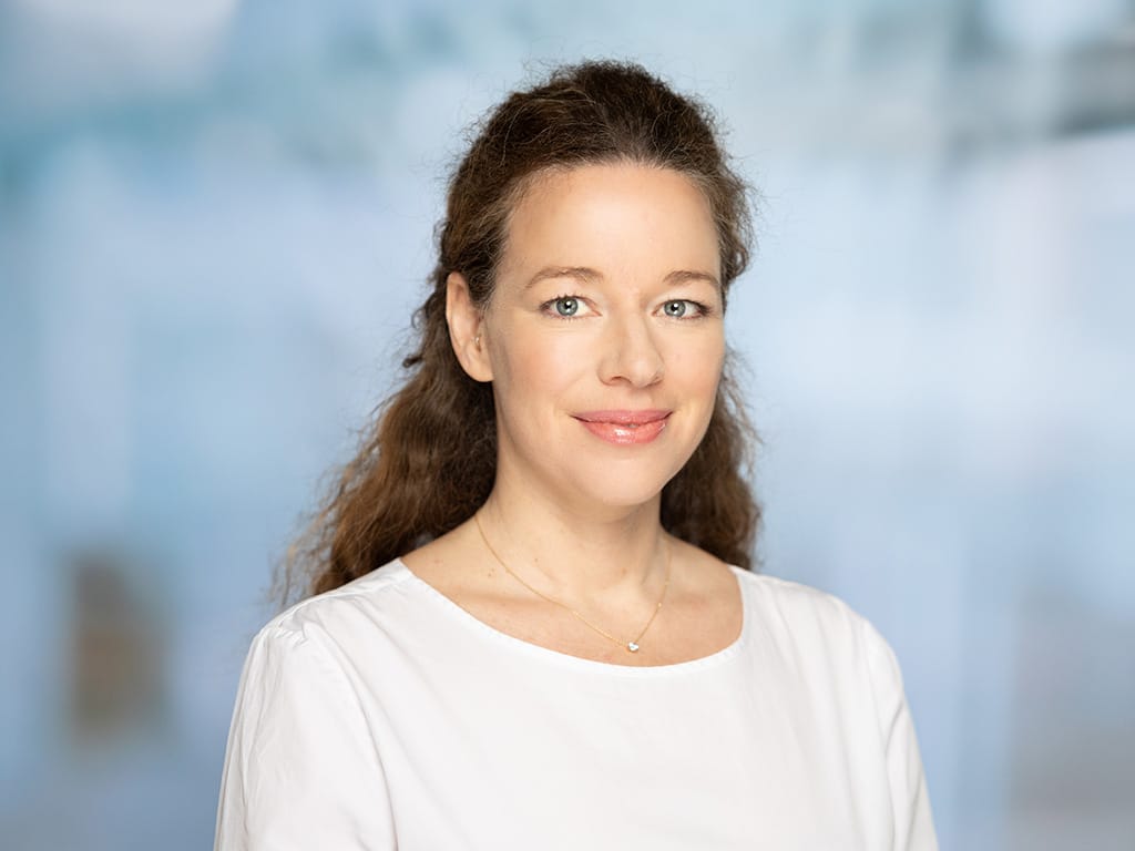 Woman with long curly hair wearing a white blouse and a small heart necklace