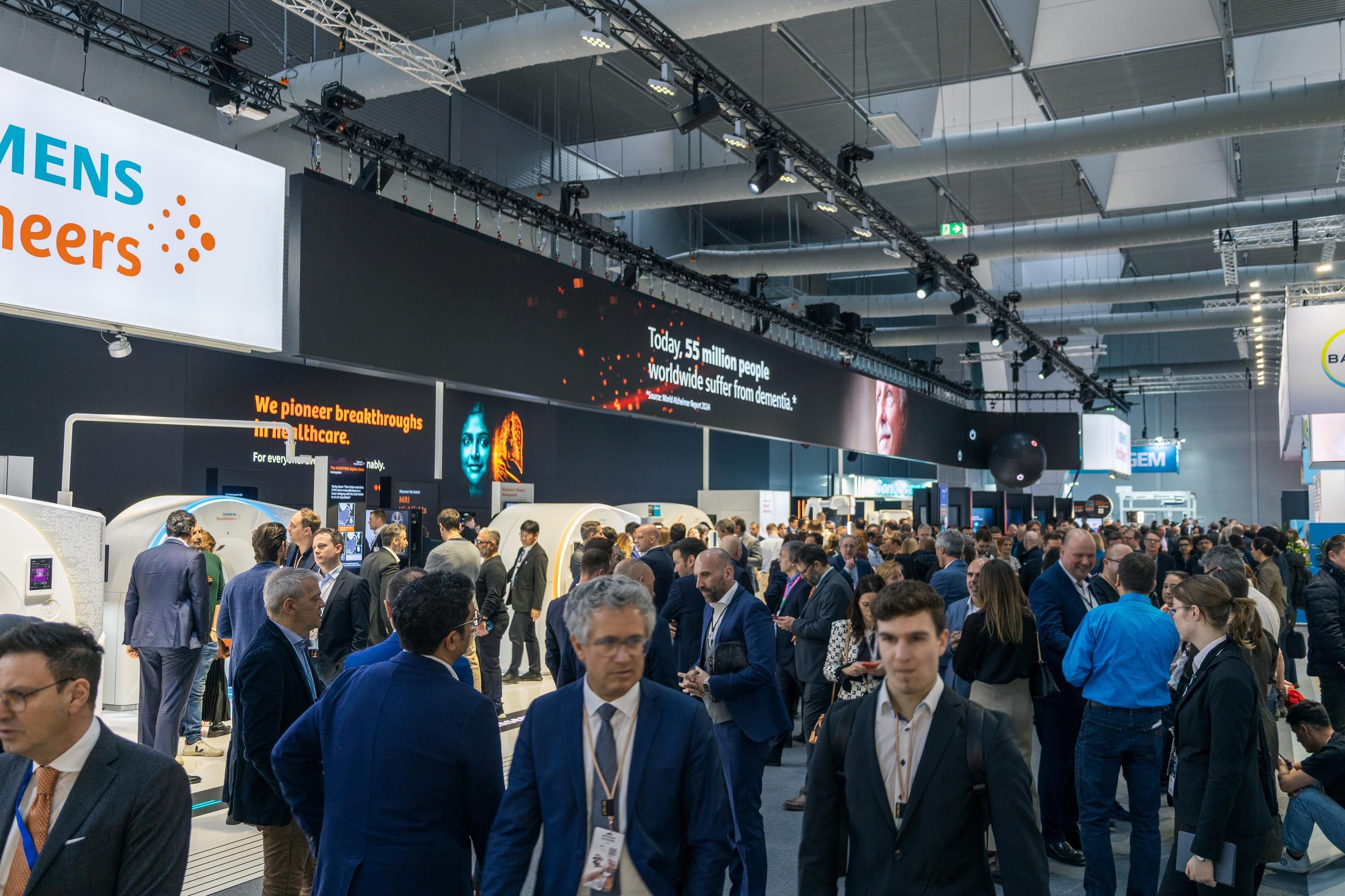 Crowded exhibition hall with Siemens Healthineers booth and dementia awareness message above.