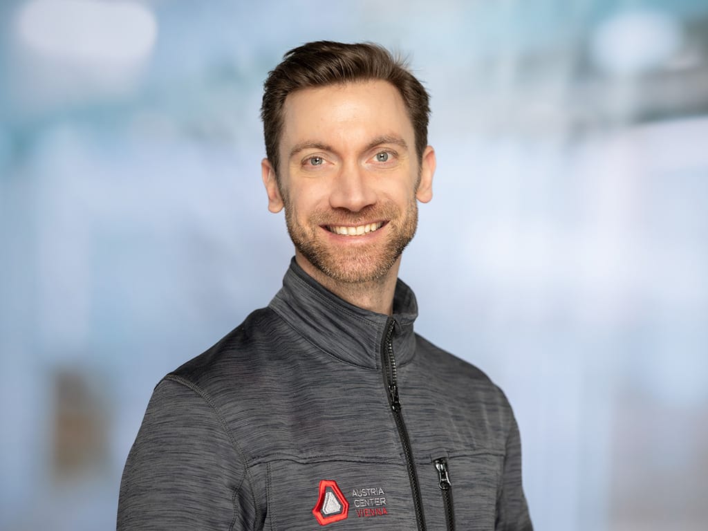 Man wearing a gray zip-up jacket with Austria Center Vienna logo on chest
