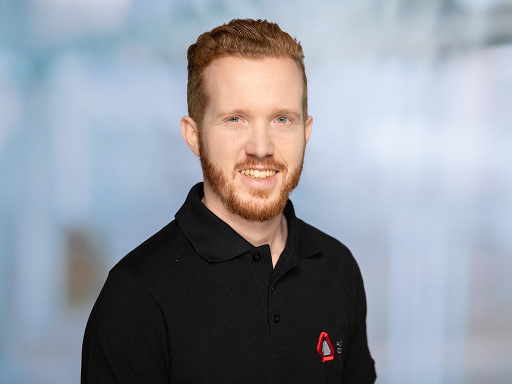 Man wearing black polo shirt with red and white logo on left chest against blurred background