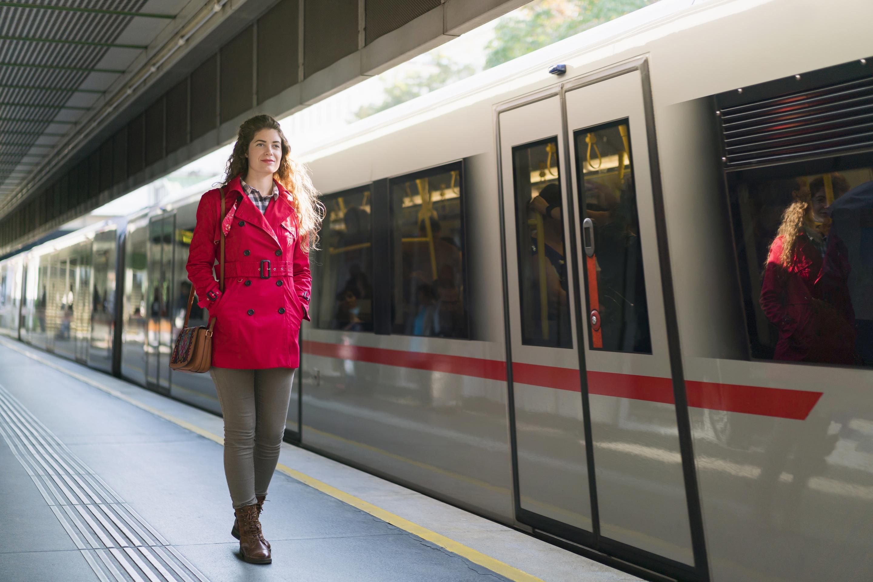 Woman in red coat standing on train platform next to a white train with red stripe