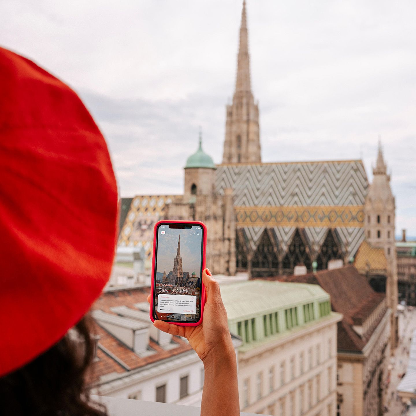 Person mit roter Mütze hält Smartphone mit Bild des Stephansdoms in Wien