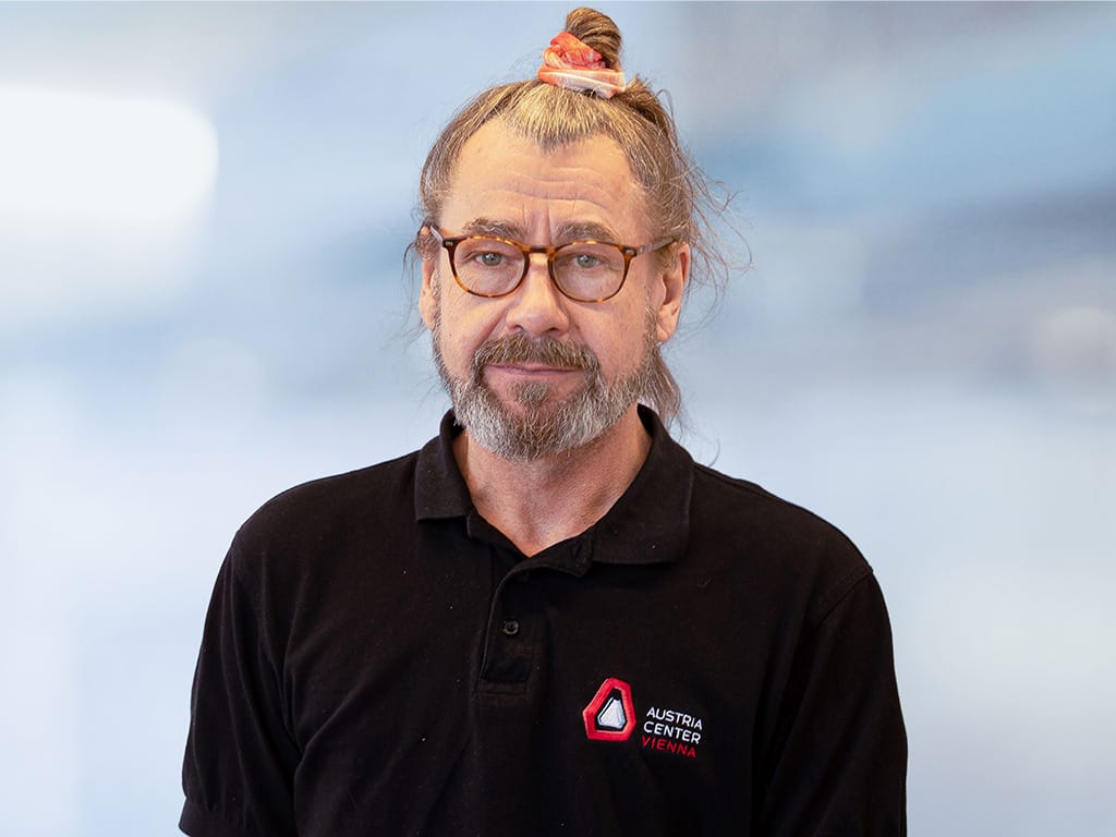 Person wearing black polo shirt with Austria Center Vienna logo on chest against blurred background