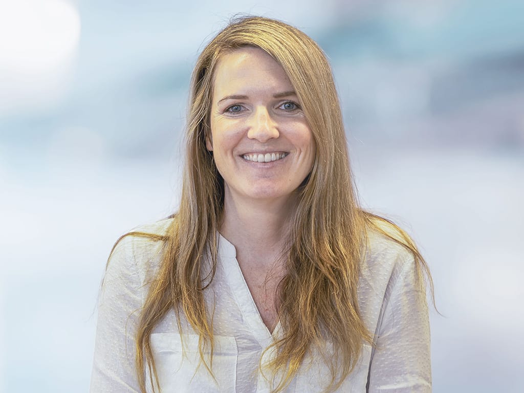 Person with long blonde hair wearing a white textured blouse against a blurred background