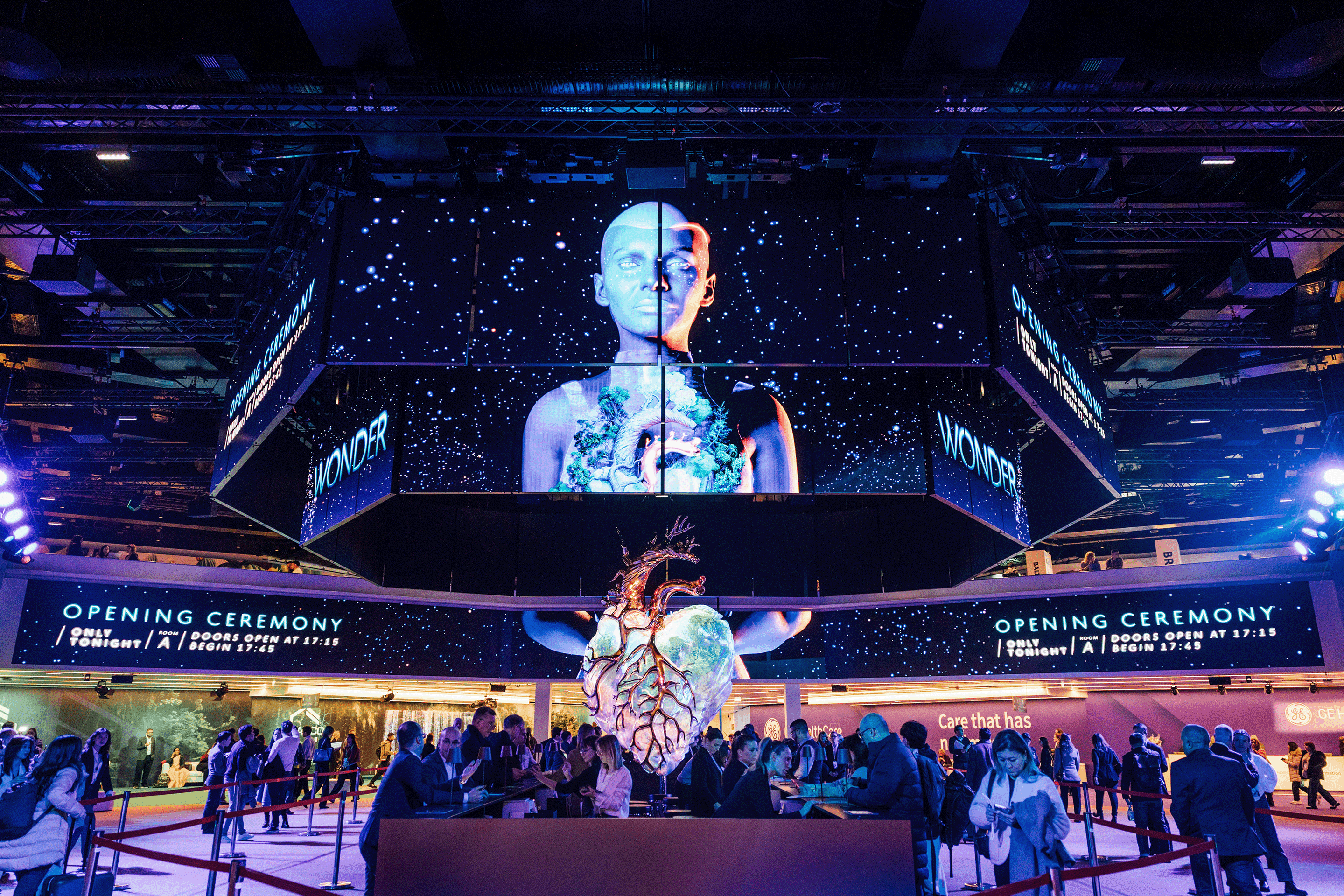 Große Herzskulptur vor digitaler Leinwand mit Text „OPENING CEREMONY“ und Menschenmenge