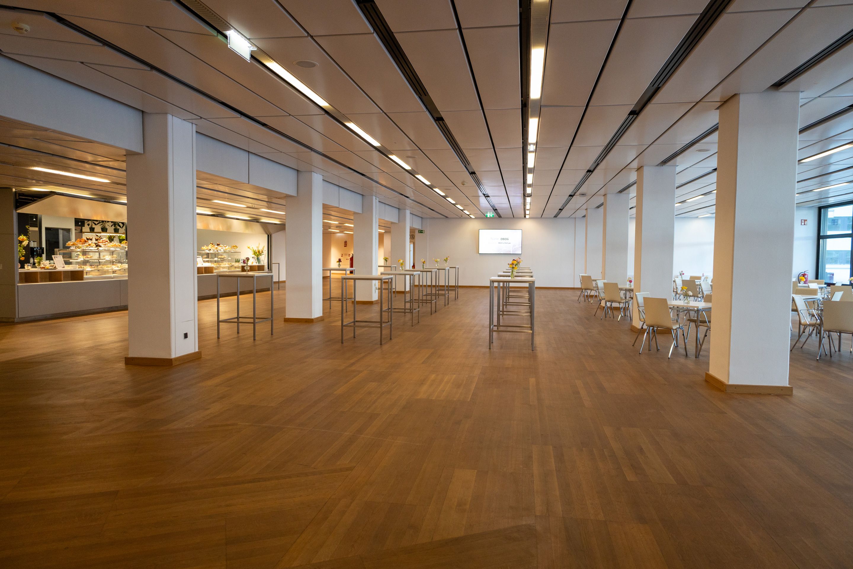 Helles Foyer mit Holzfußboden, weißen Säulen und Stehtischen.