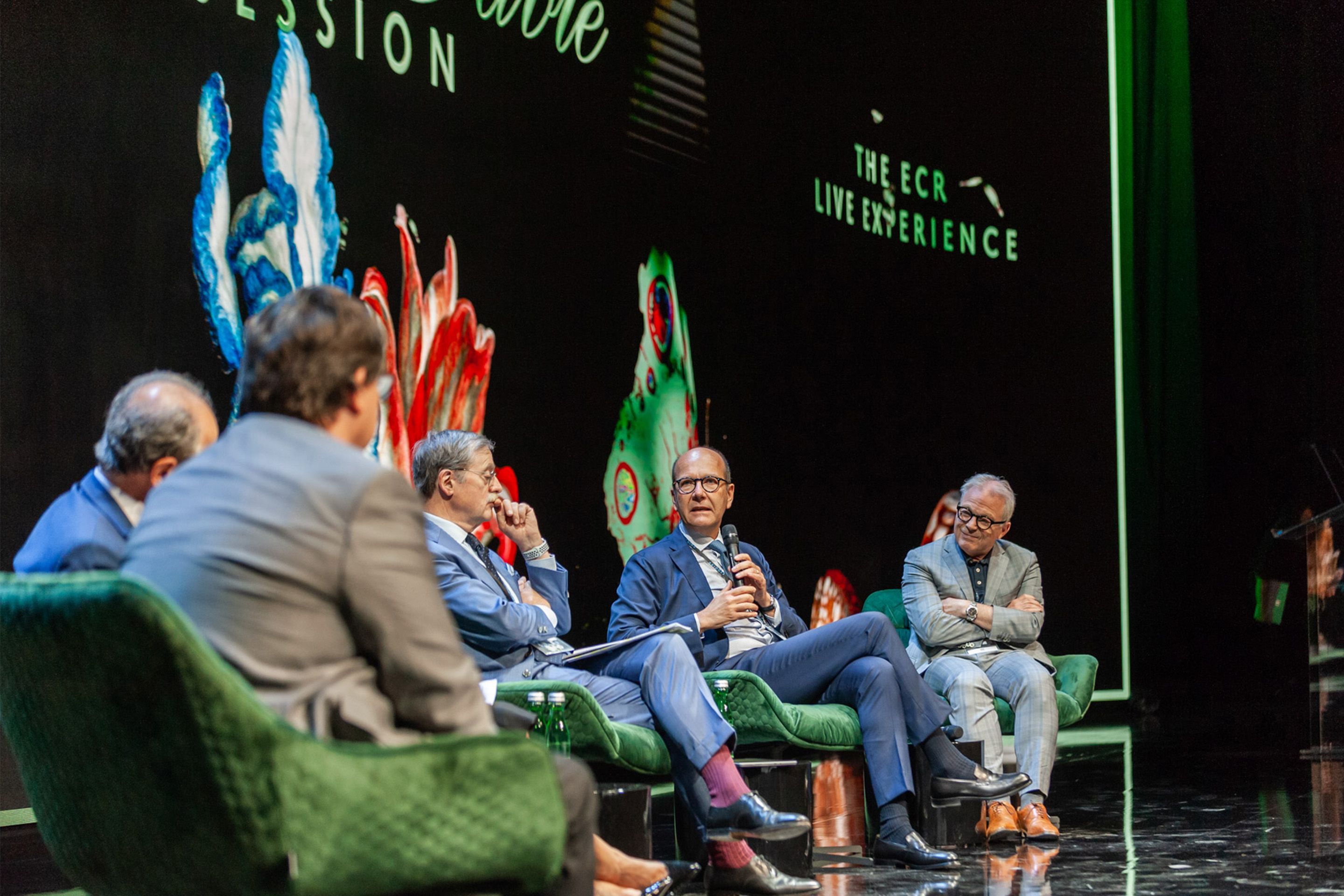 Foto: Podiumsdiskussion auf Bühne mit schwarzem Hintergrund und natürlichen Motiven