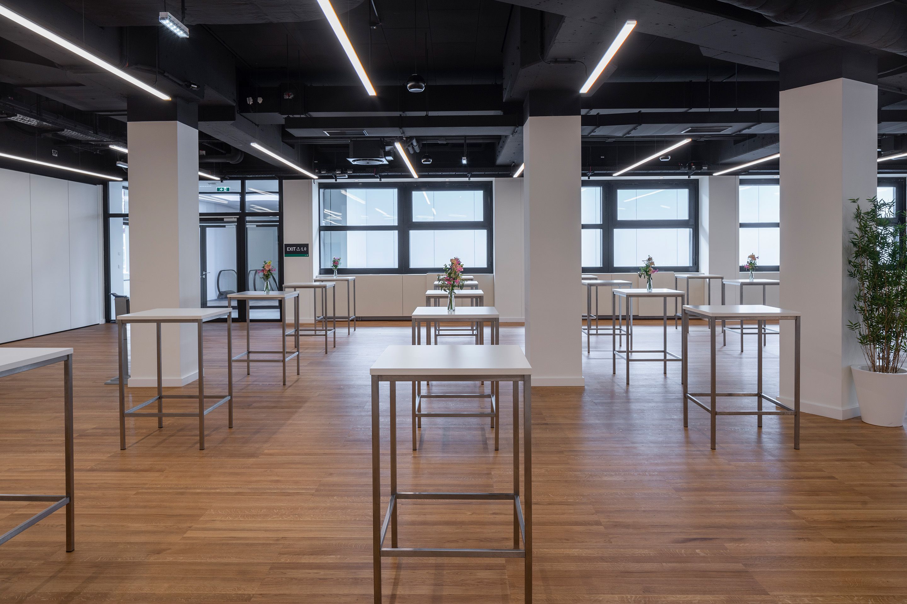 Foto: weißes Foyer mit Hochtischen, Blumenschmuck, dunkle Decke, Holzboden