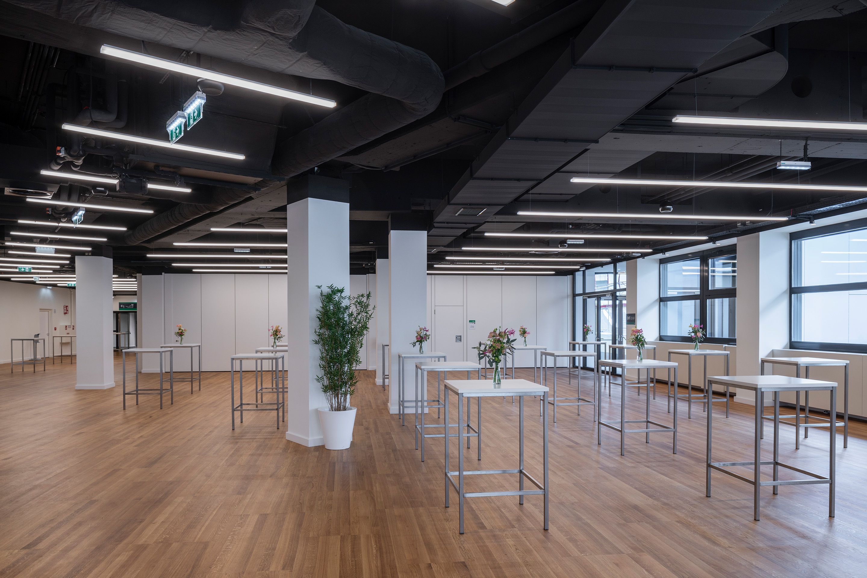 Foto: weißes Foyer mit Hochtischen, Blumenschmuck, dunkle Decke, Holzboden