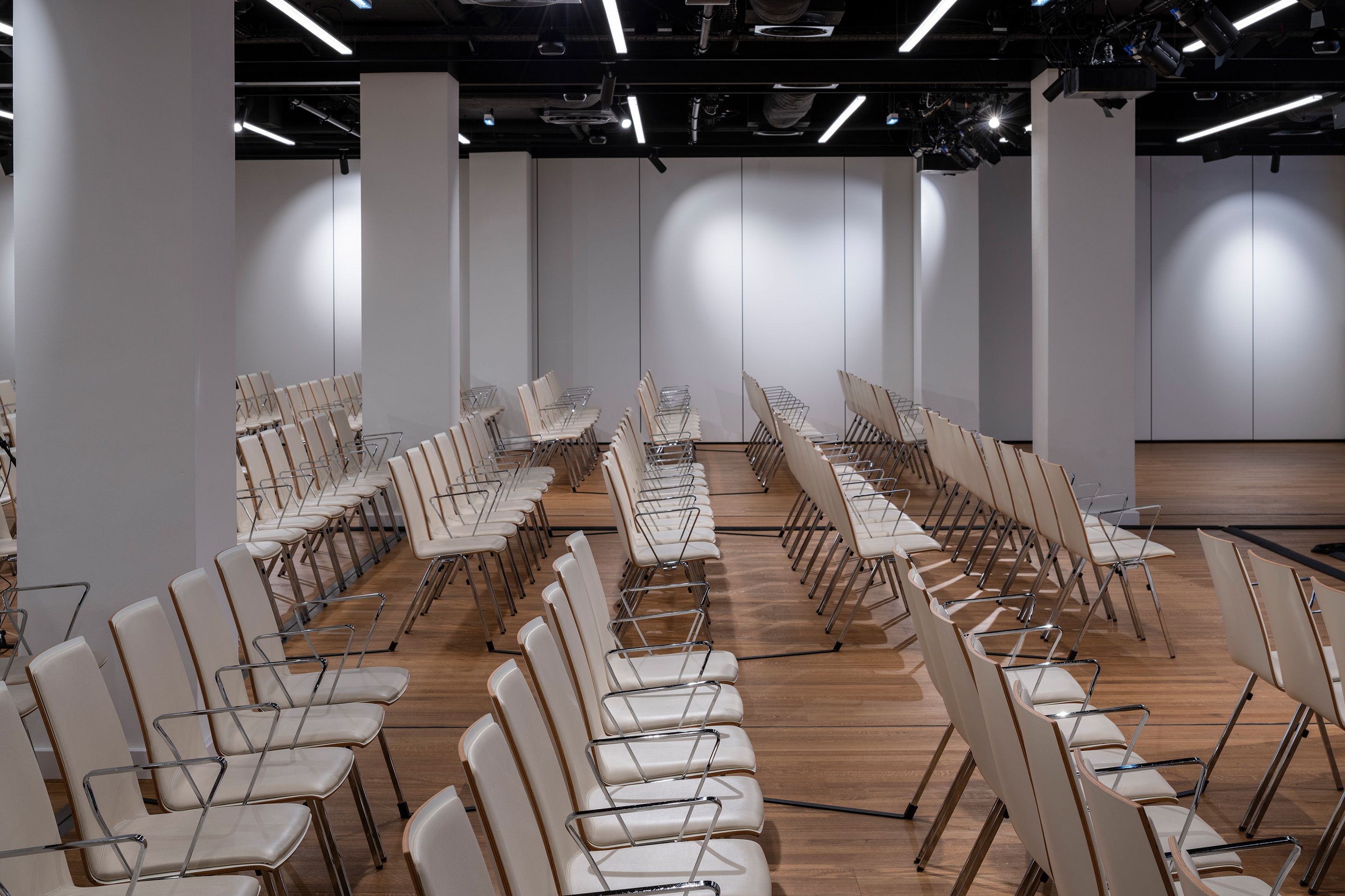 Foto: Sitzreihen in einem Saal mit Holzboden, beleuchtete Wand