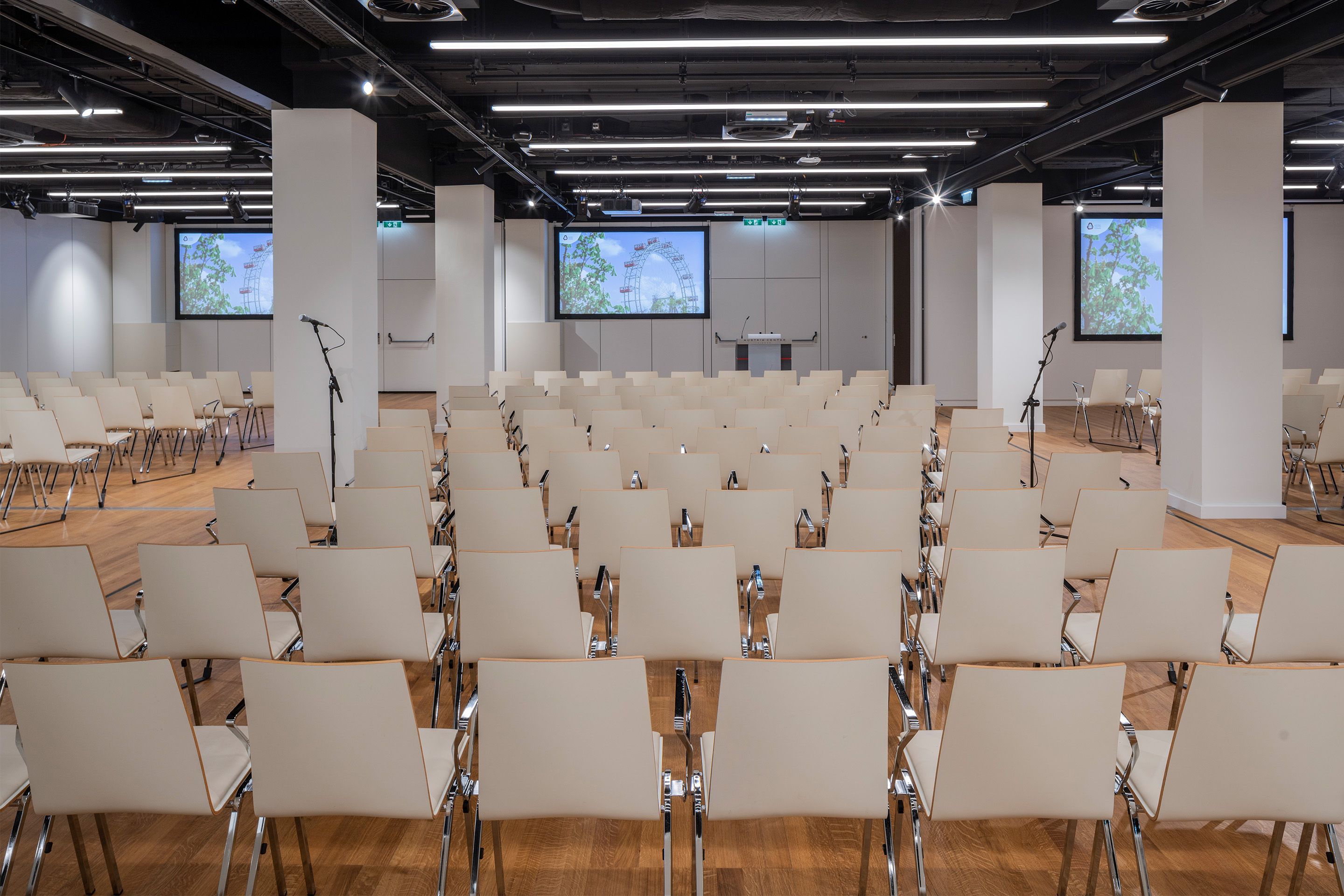 Foto: Sitzreihen in einem Saal mit Holzboden, Monitore