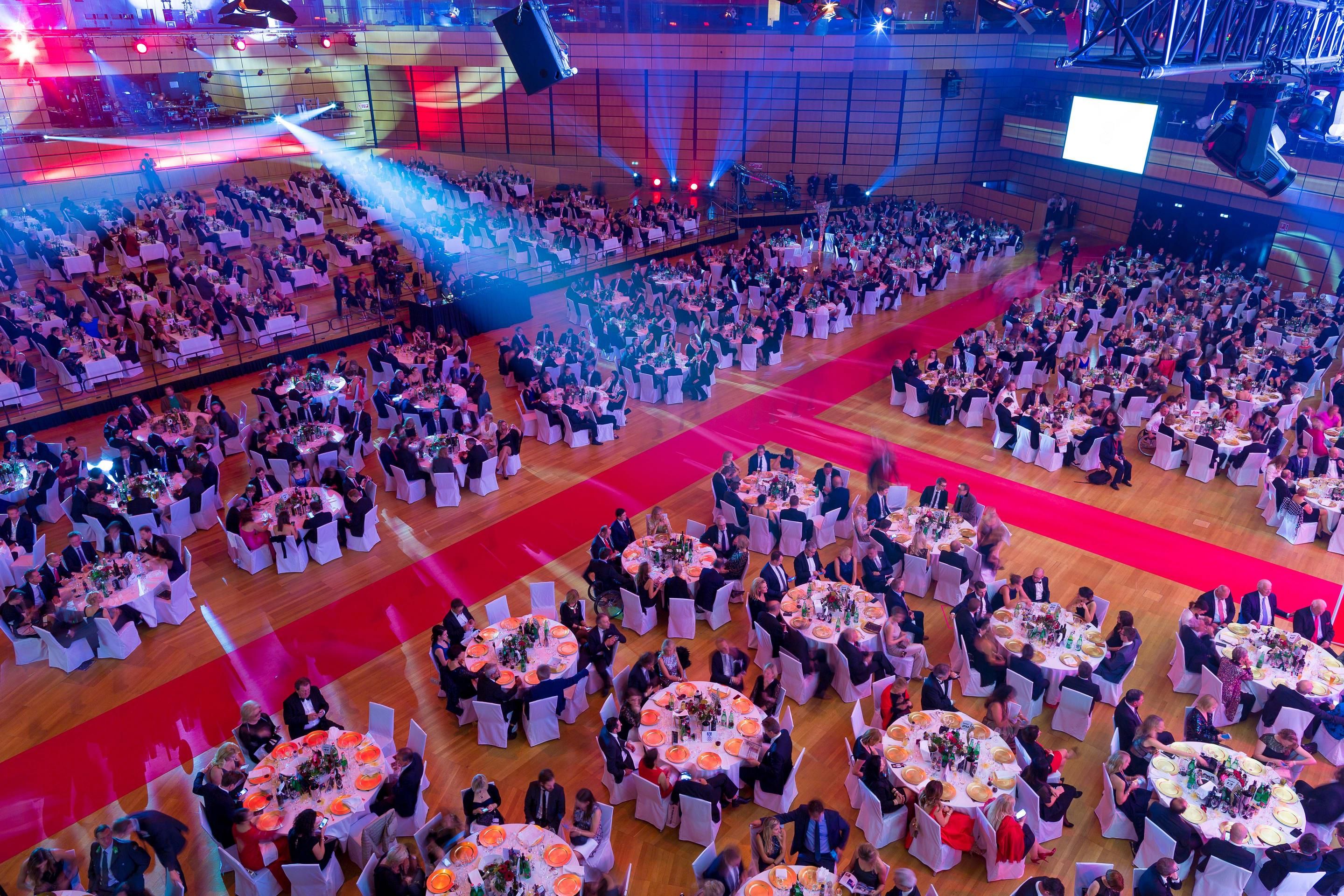 Foto: Menschen in einer Halle auf Gala-Tischen, roter Teppich