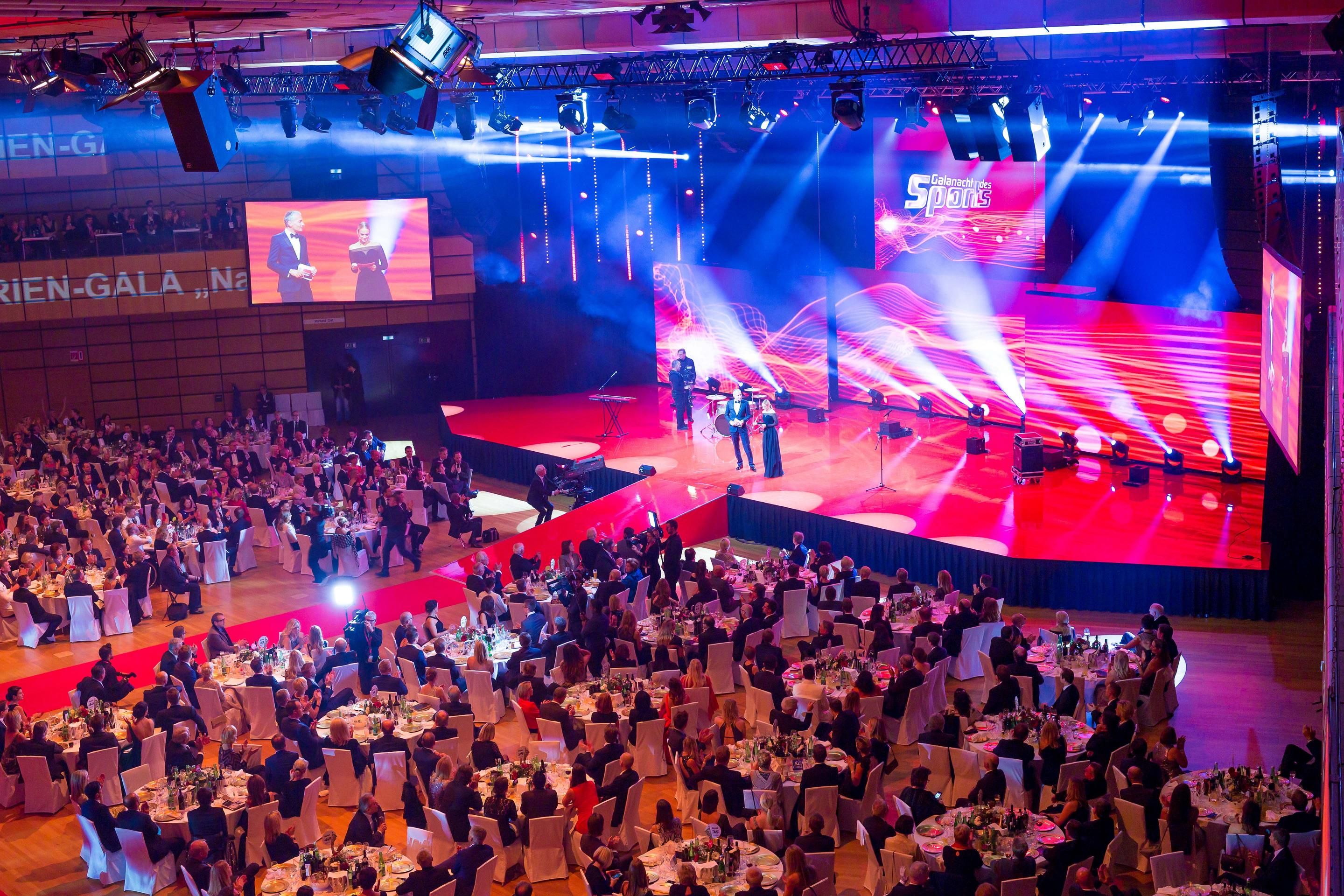 Foto: Menschen in einer Halle vor einer roten Buehne, Gala-Bestuhlung