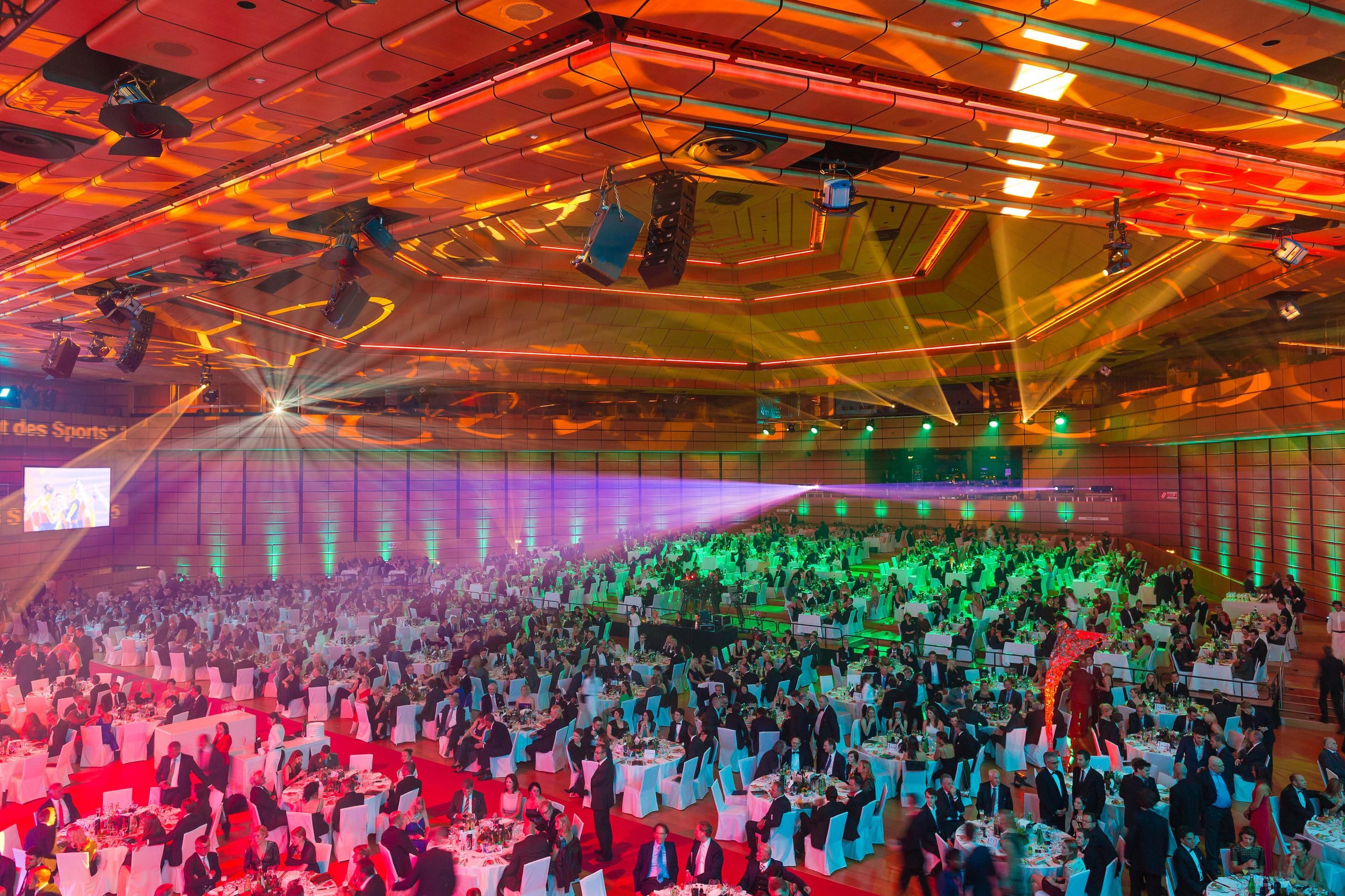 Foto: Menschen in einer Halle mit bunten Lichtern in Gala-Bestuhlung