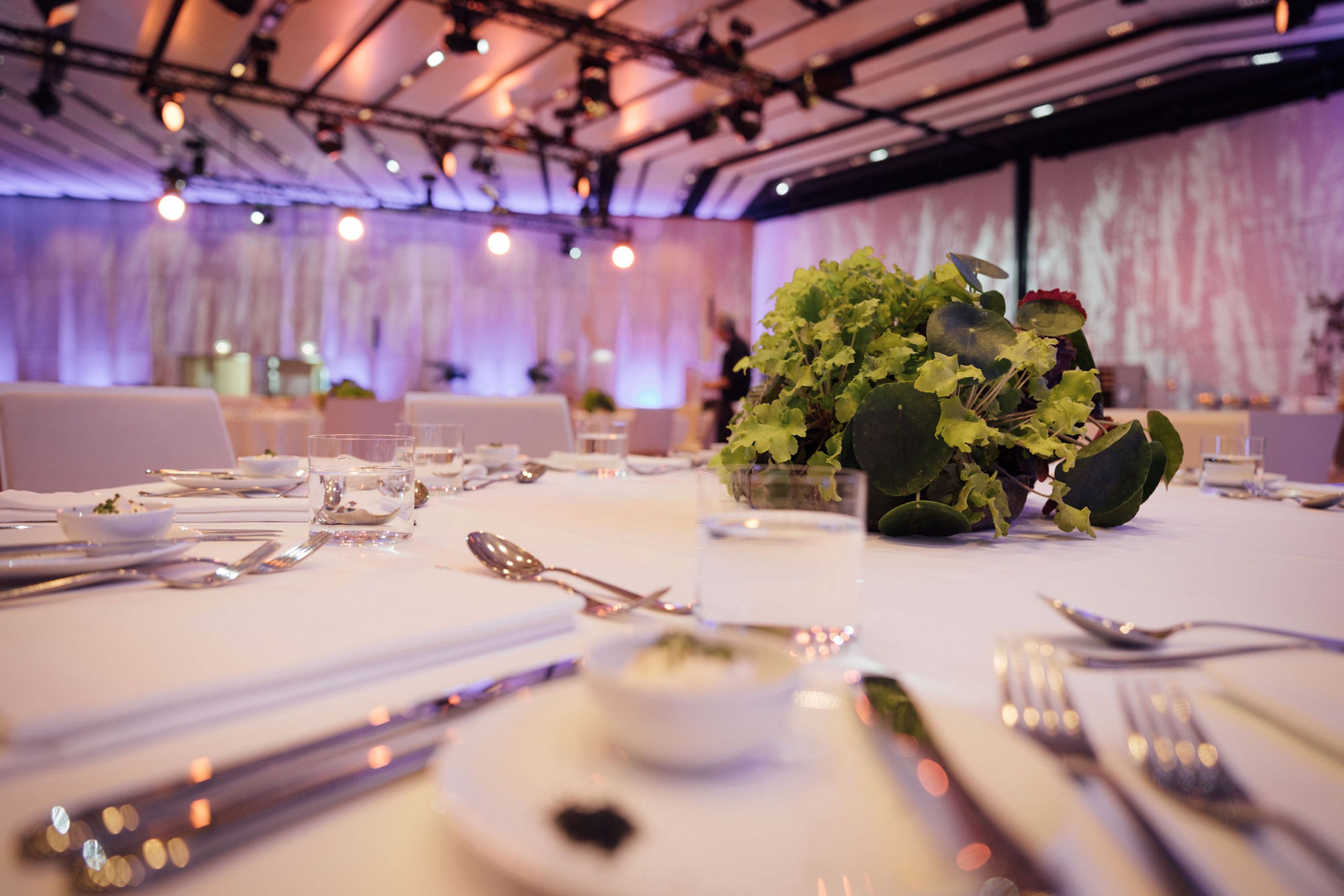 Foto: Runder gedeckter Tisch mit Pflanzendeko, ein Mensch im Hintergrund
